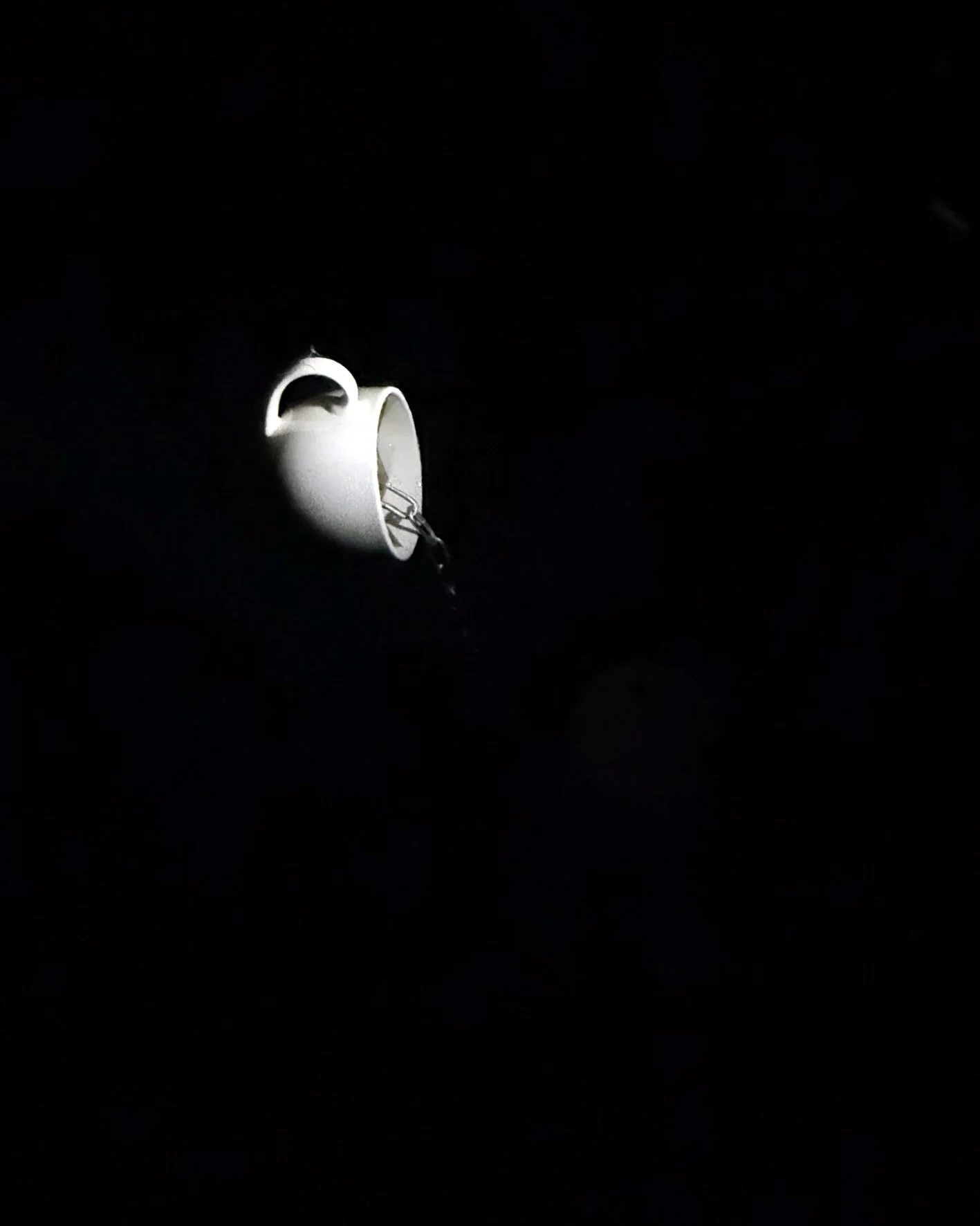 A white ceramic mug lying on its side in a dark environment, with a chain attached to its handle.