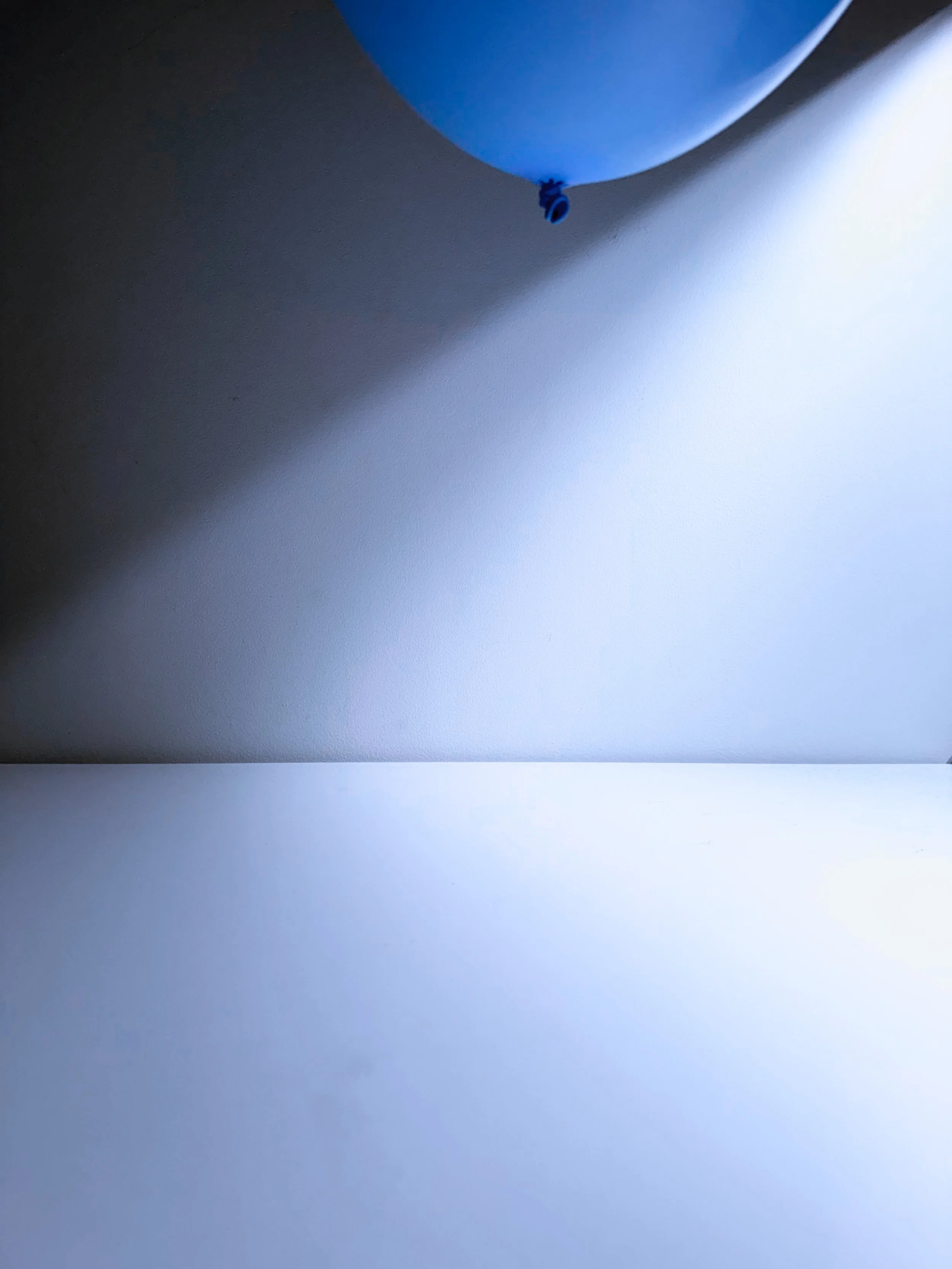 Close-up of a blue balloon against a wall with shadows.