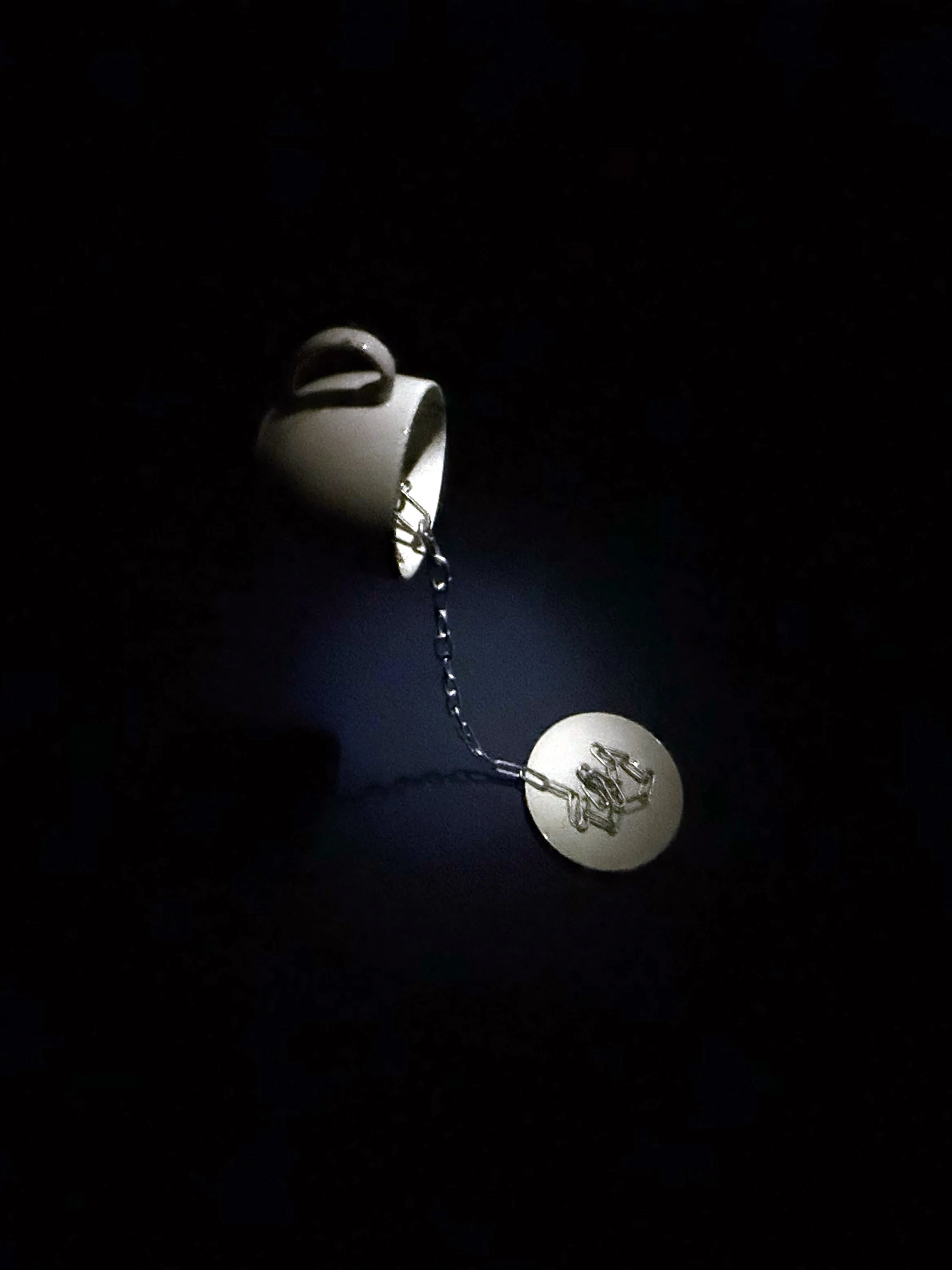 Close-up of a silver necklace with a circular pendant featuring a bicycle engraving, hanging against a dark background.