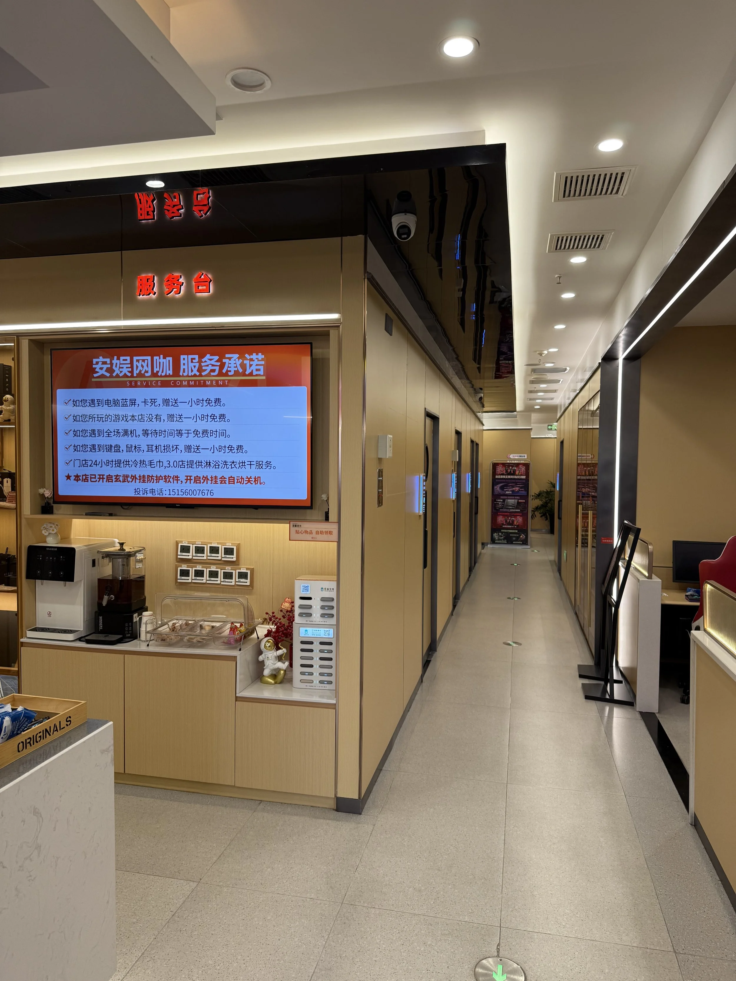 Interior view of a service area in a building with a digital display screen, ceiling lights, and an elevator hallway with multiple floors.