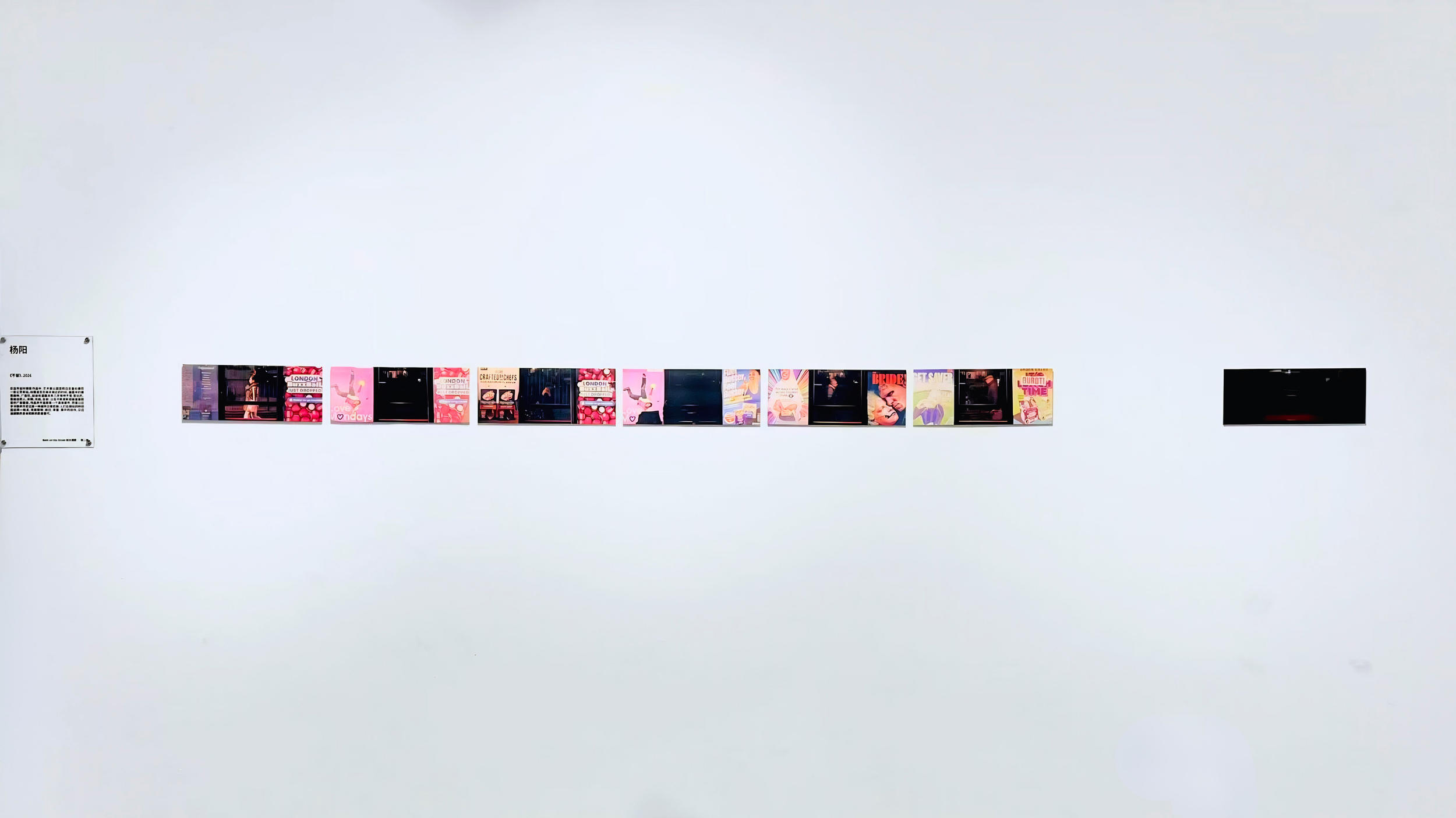 A white gallery wall with a series of small, colorful photographs or posters arranged in a horizontal line, and a black monitor or screen at the far right.