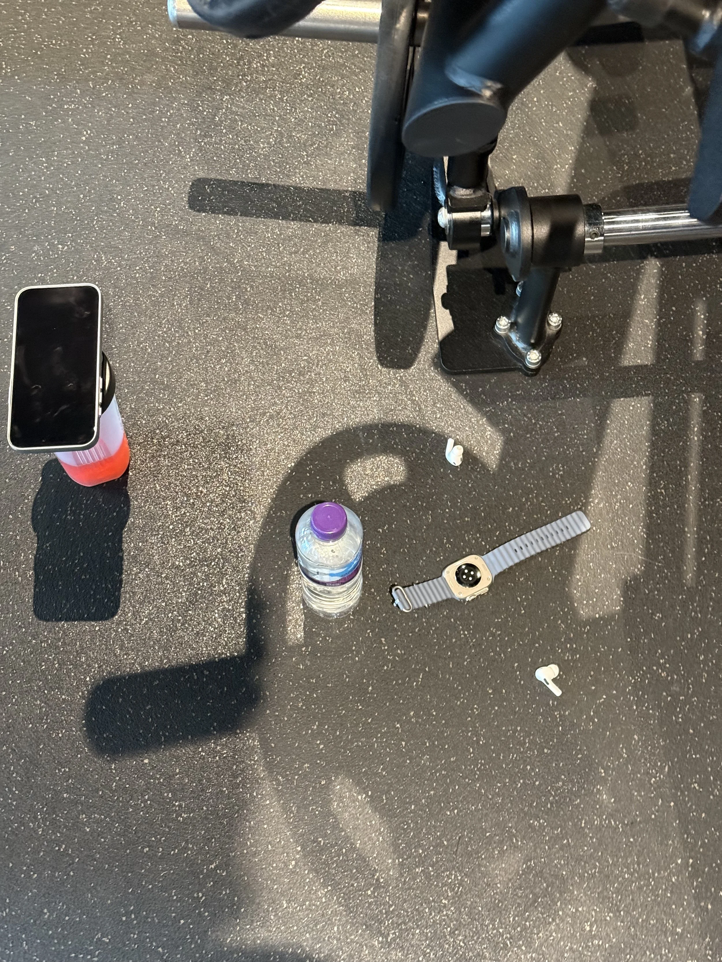 Gym floor with water bottle, smartphone on a fitness roller, headphones, and a fitness device.