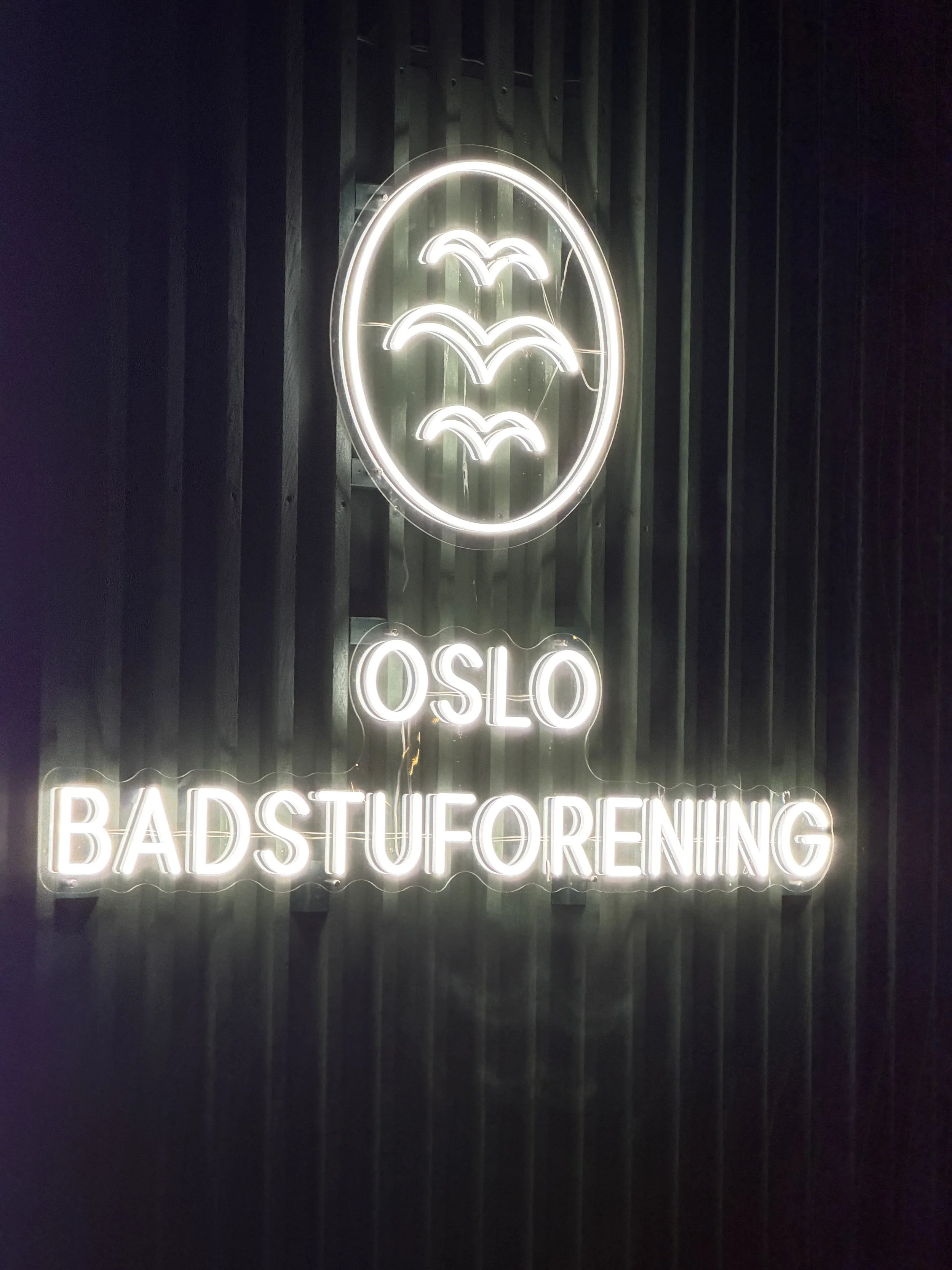 Neon sign with three birds inside an oval, above the word 'OSLO' and below the phrase 'BADSTUFORFENING'.