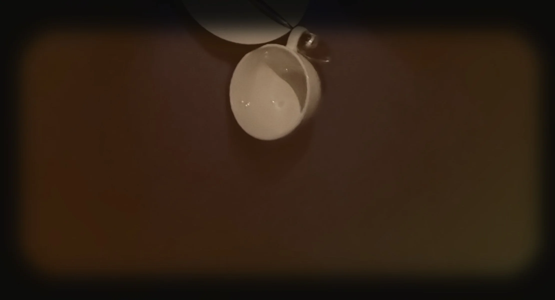 An overhead view of an open, empty white coffee cup on a dark surface with a spoon resting on the cup's rim.