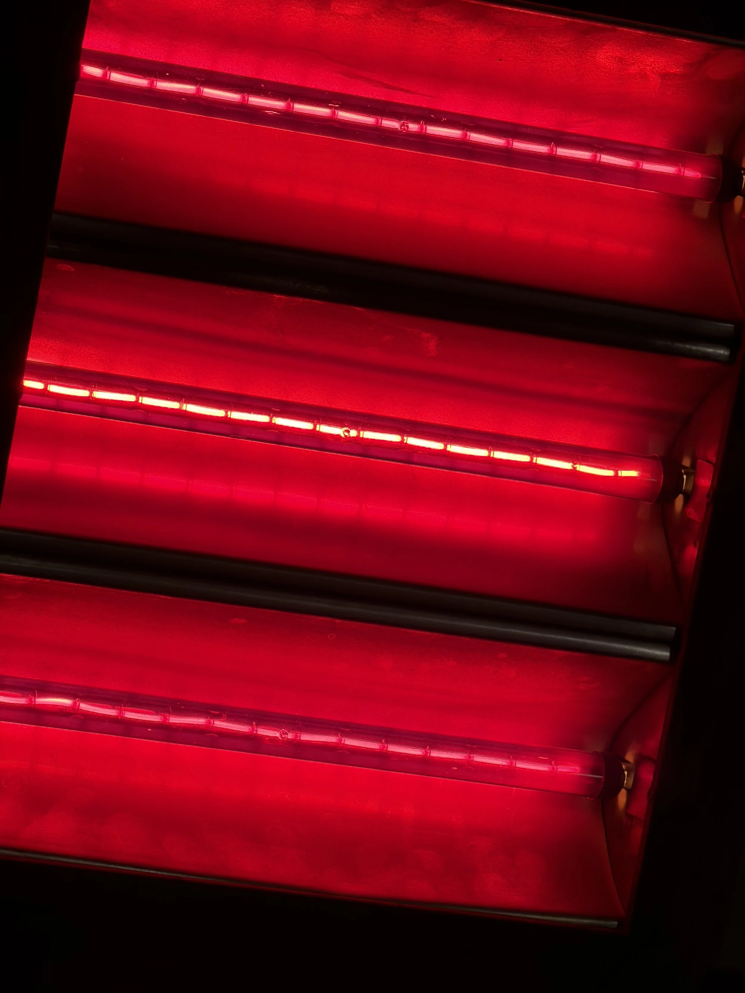Red neon lights and black rods arranged diagonally within a wooden frame, creating a modern and sleek visual.