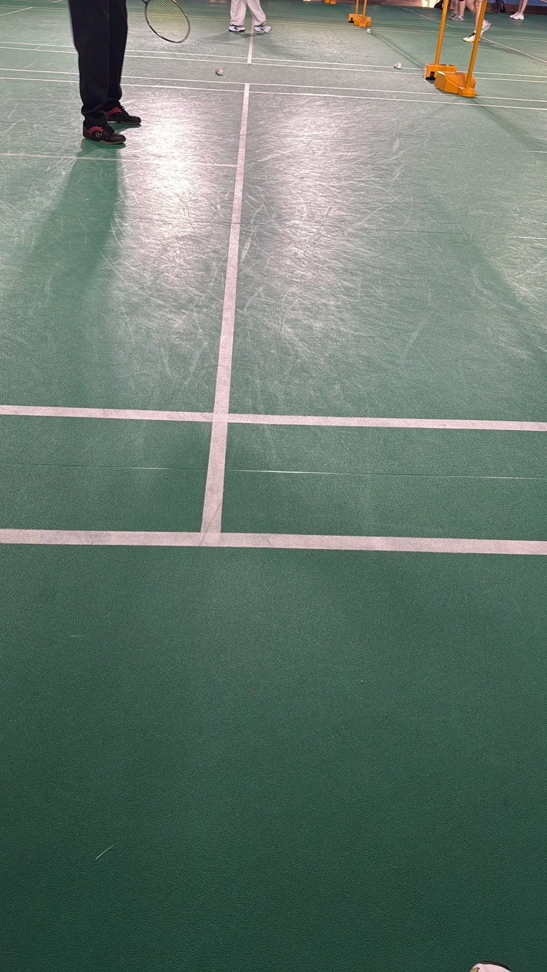 Indoor badminton court with players and equipment in the background, visible shuttlecocks and racquets.