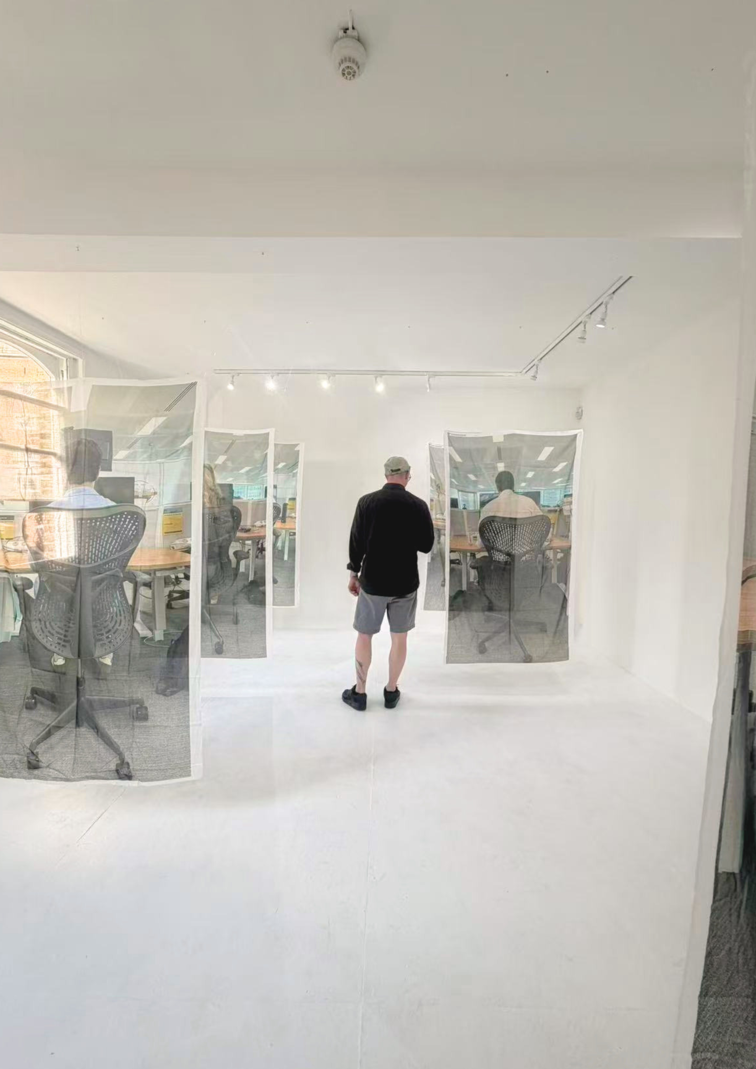 Person standing in front of a glass wall with people working on computers inside an office.