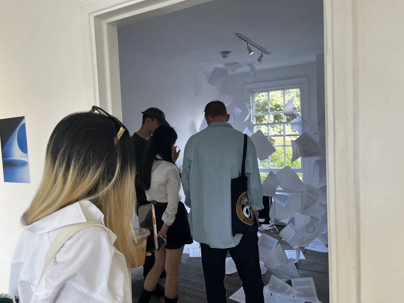 People gather in front of a window with papers flying around, possibly in a creative or staged scene.