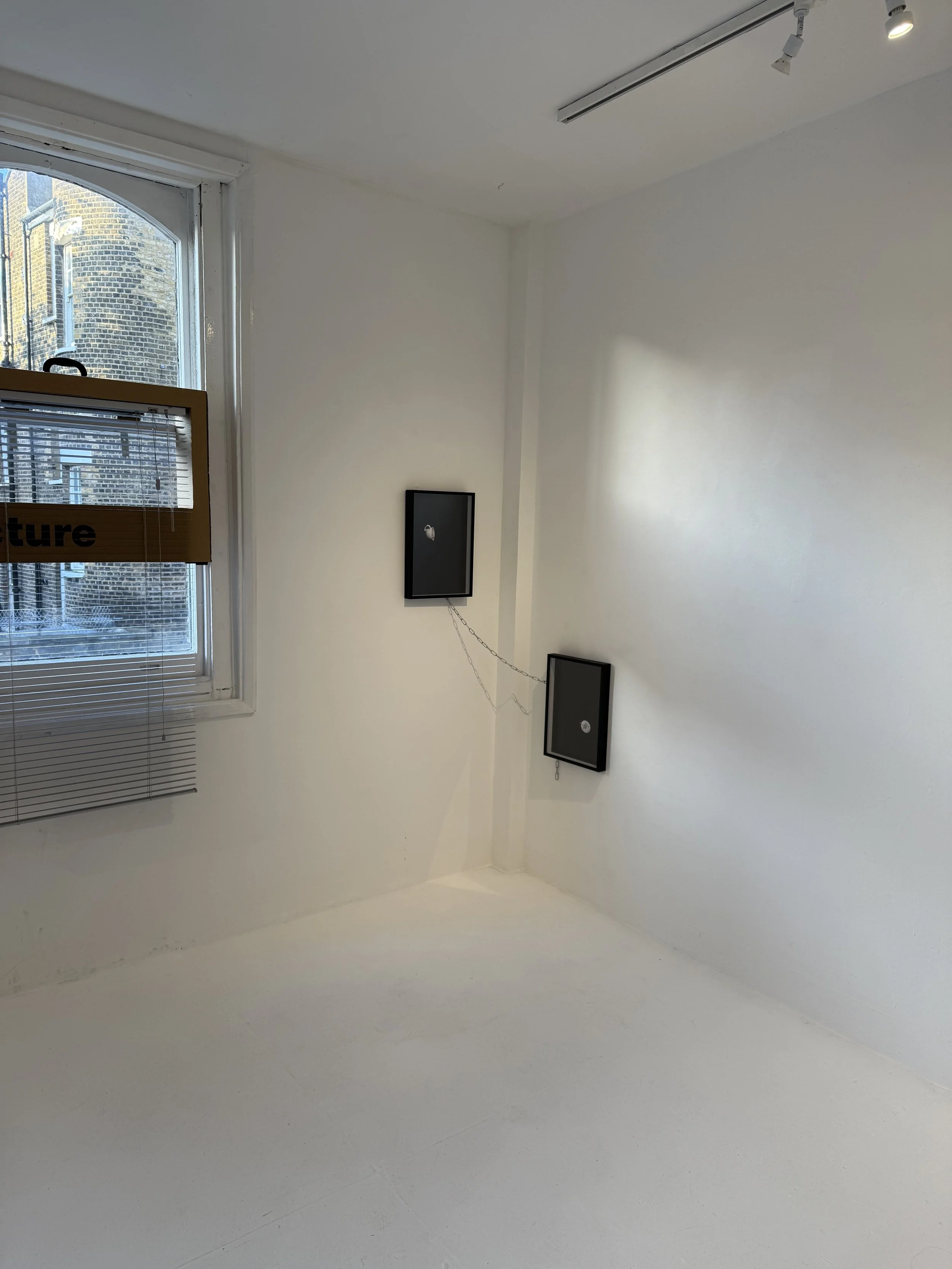 An art gallery with white walls and a white floor, wall-mounted frames, and a window with blinds.