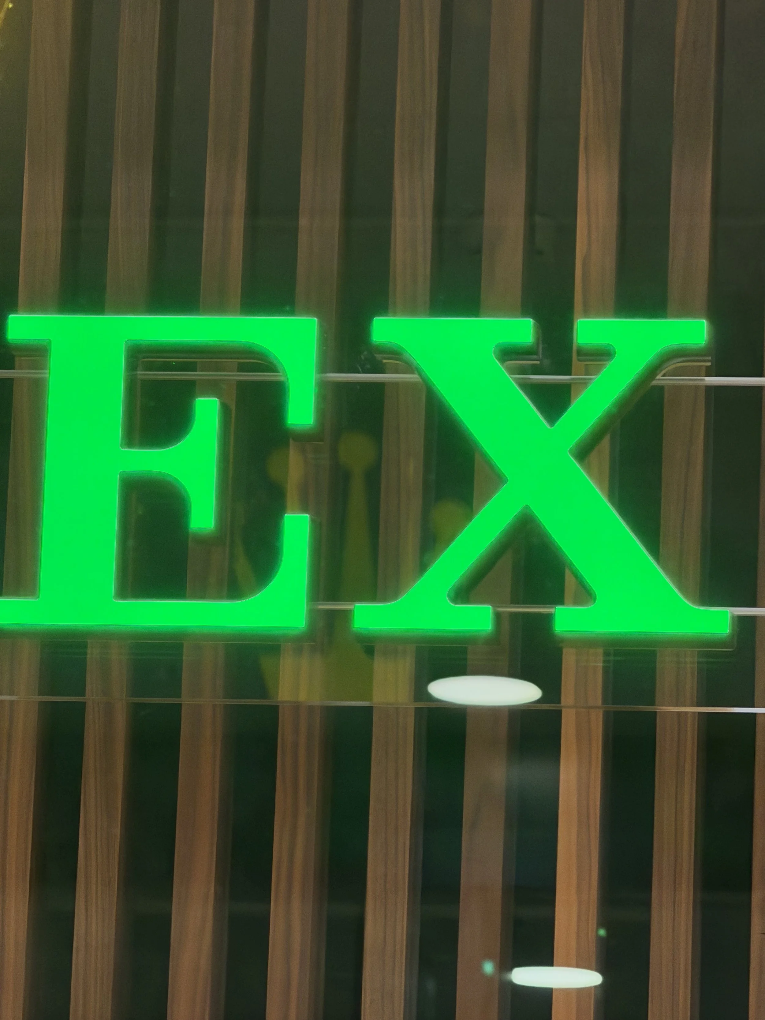 Green illuminated the letter X against a wooden slat wall.
