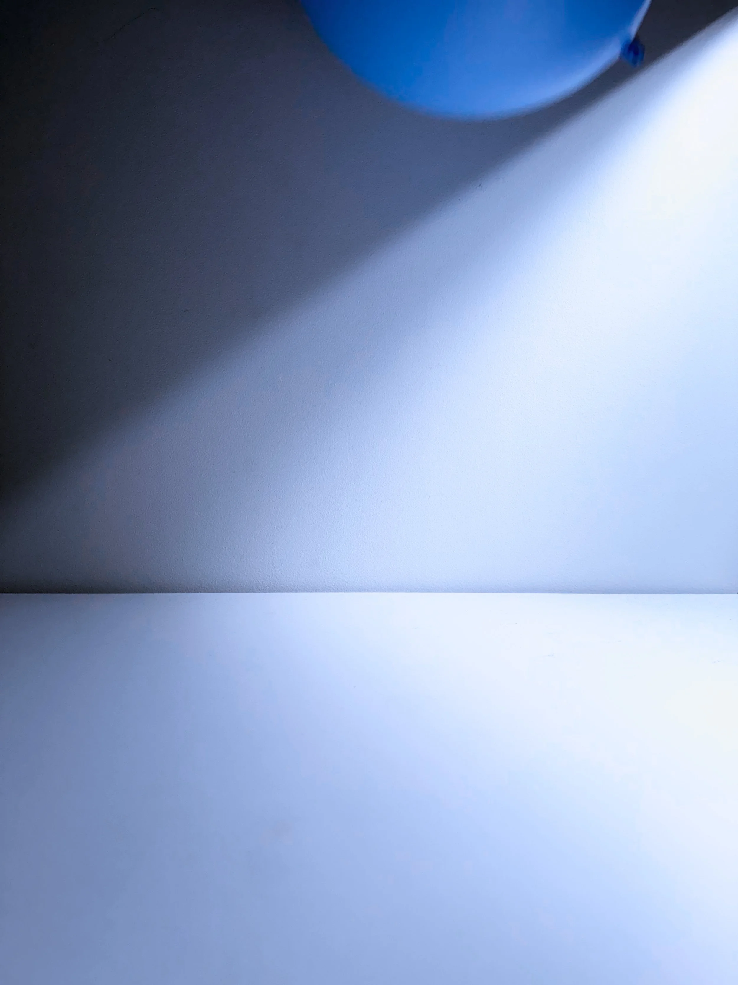 Close-up of a wall with a faint shadow cast by an object or person, and part of a blue object or surface at the top edge.