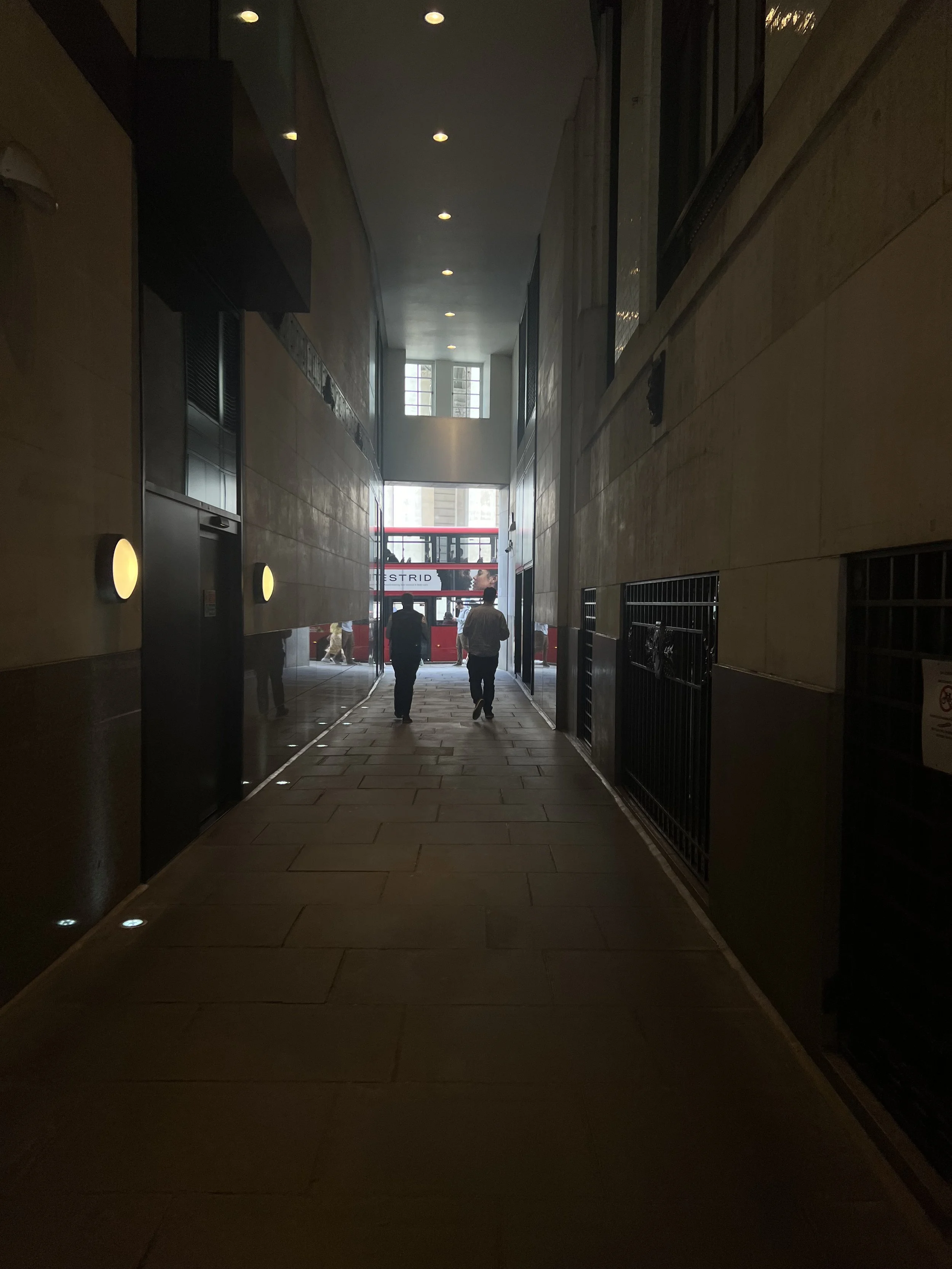 A dimly lit hallway leading to a bright outdoor area with a double-decker bus and people walking.