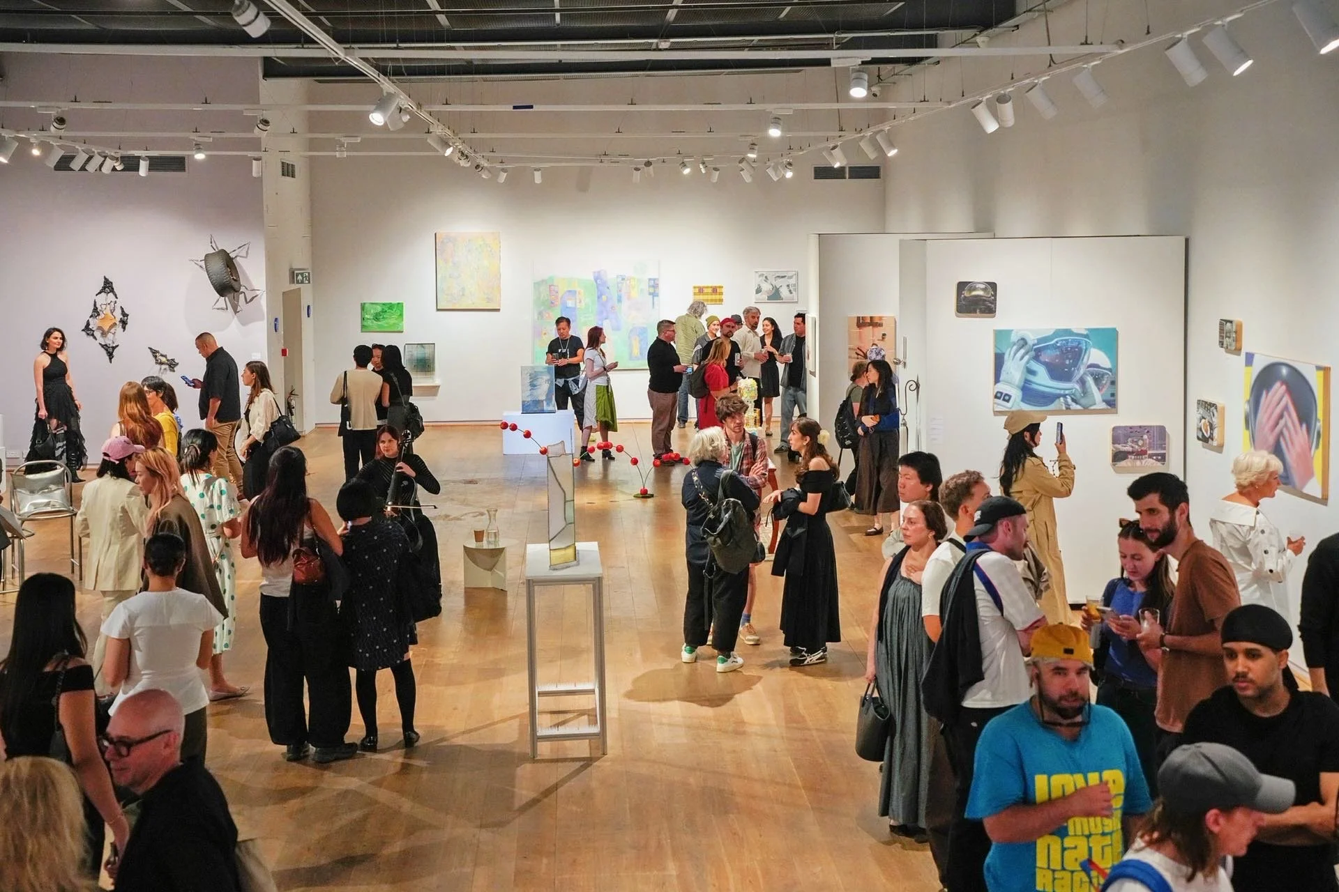 People viewing and discussing artwork at an art gallery or museum exhibit, with various paintings and sculptures on display.