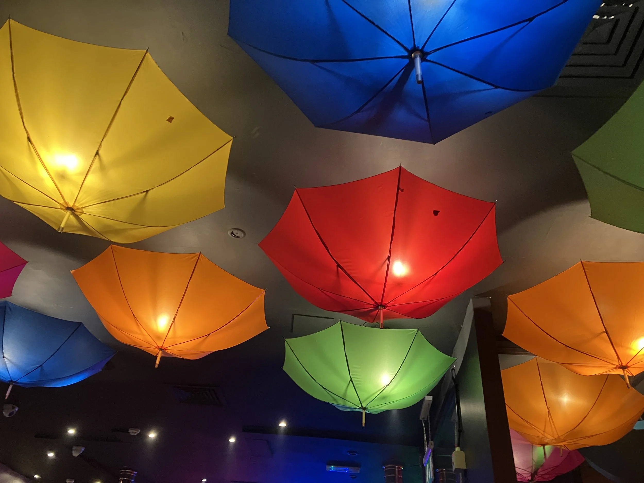 Colorful umbrellas hanging upside down from the ceiling, illuminated with lights.