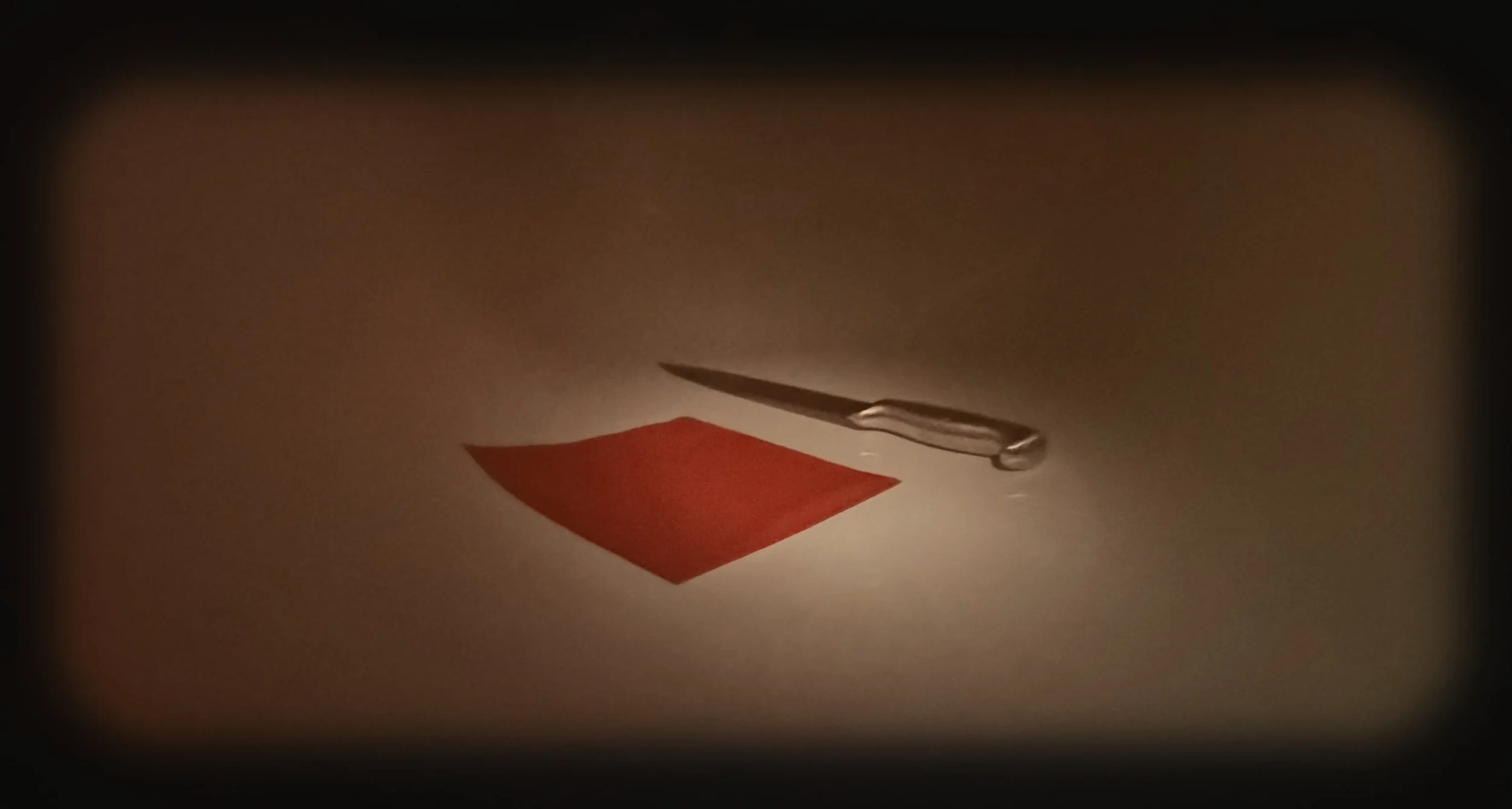 A sewing needle piercing through a piece of red fabric on a white surface, with a small drop of clear liquid next to it.