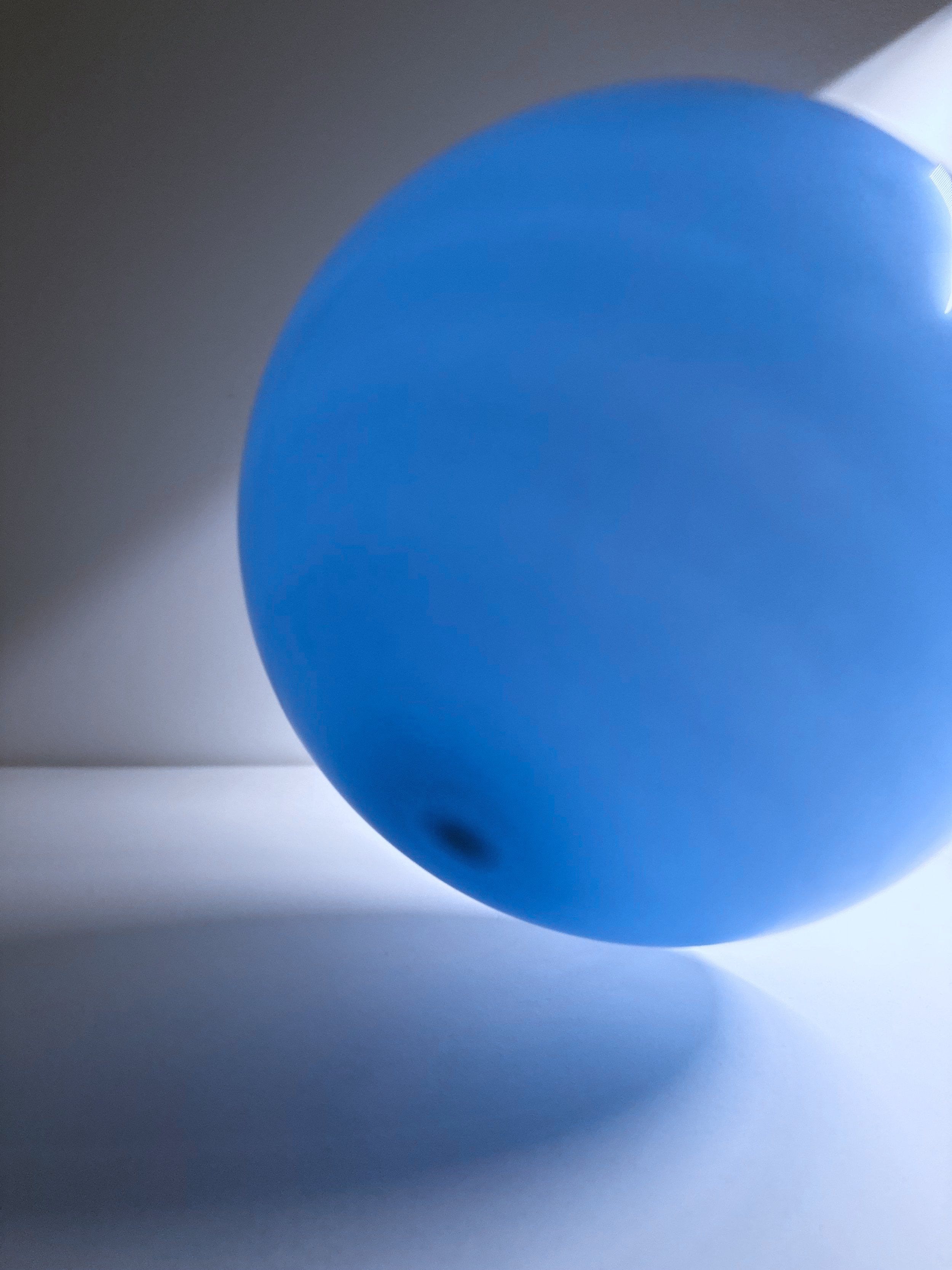 Close-up view of a blue balloon with light reflections on its surface, set against a dark background with the balloon casting a shadow.