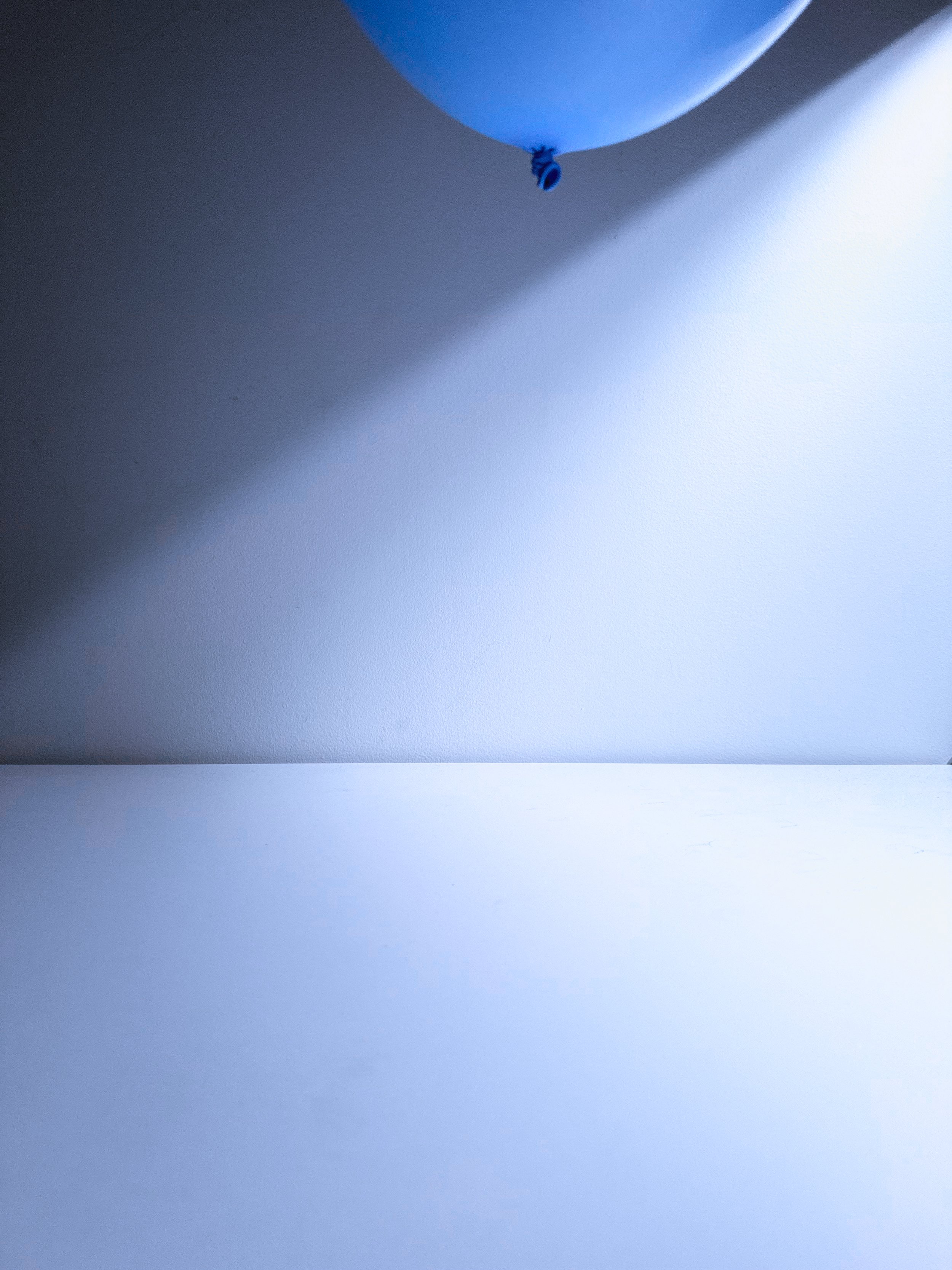 A light blue balloon floating against a white wall, casting a shadow.