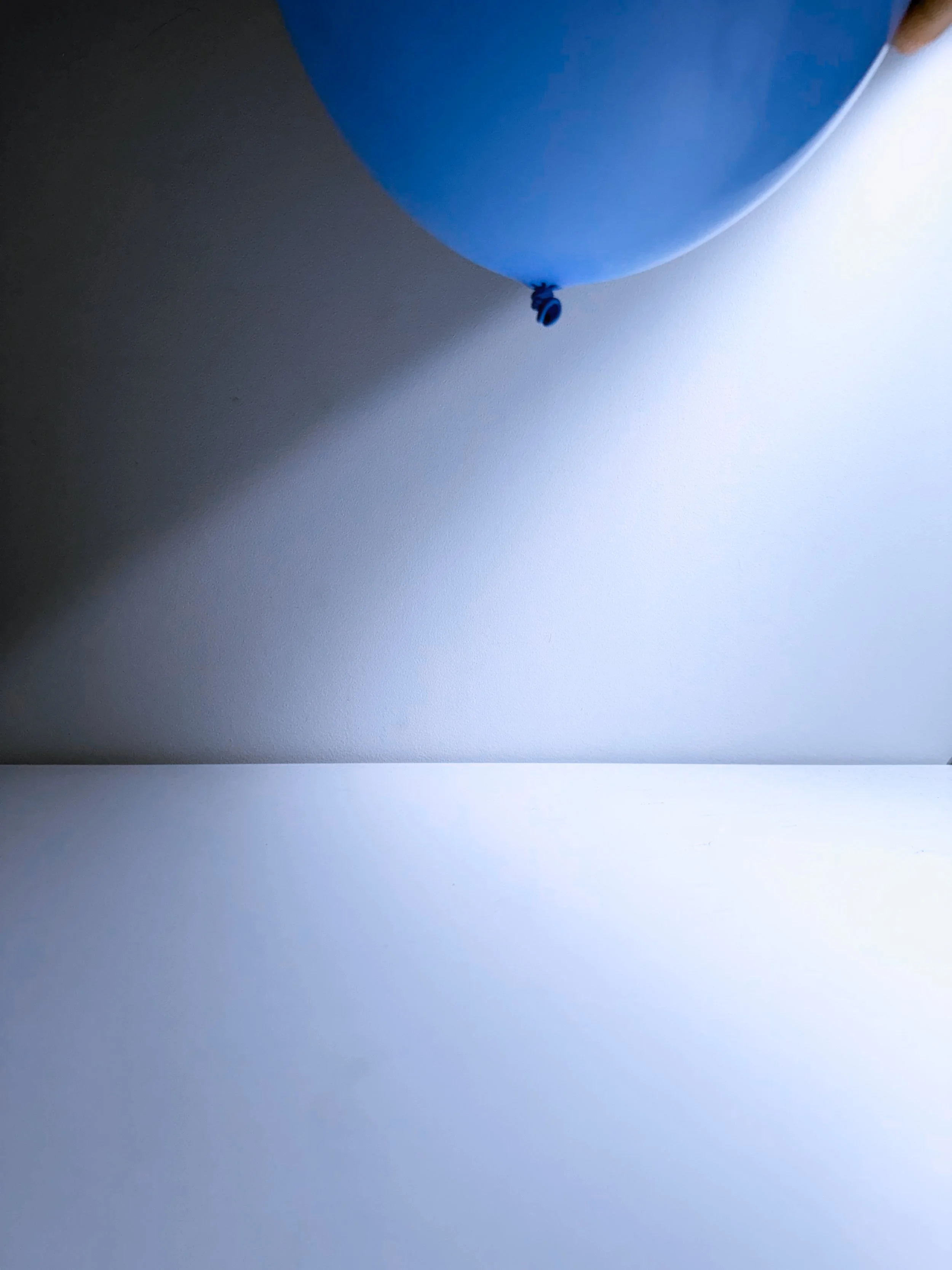 A blue balloon partially visible at the top of the image, with the bottom tied off with a knot, against a background of white and gray surfaces.