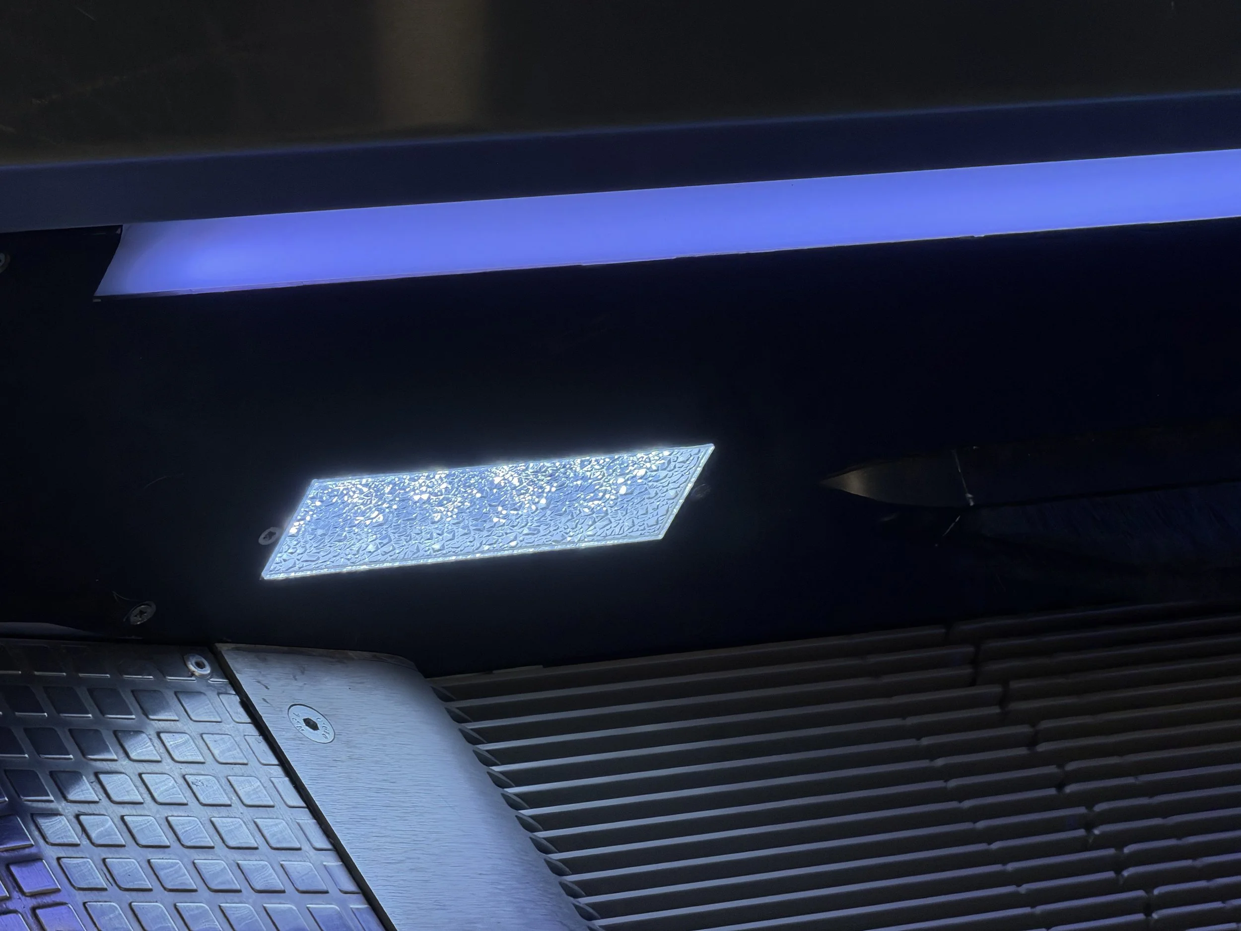 Close-up of a laptop keyboard with a blue light strip above it, showing a portion of the keyboard and a textured, illuminated surface.