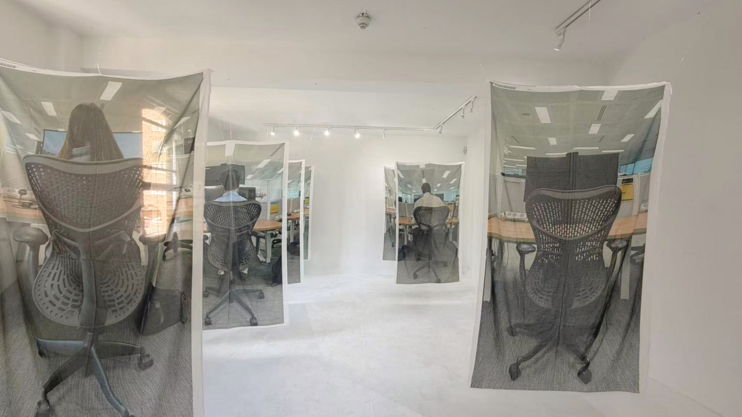 A room with glass panels featuring printed images of office chairs and desks, creating a visual effect of multiple office scenes.