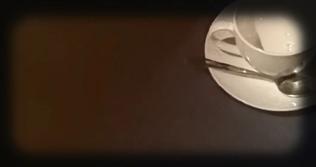 Partially visible white cup and saucer with a spoon on a dark surface.