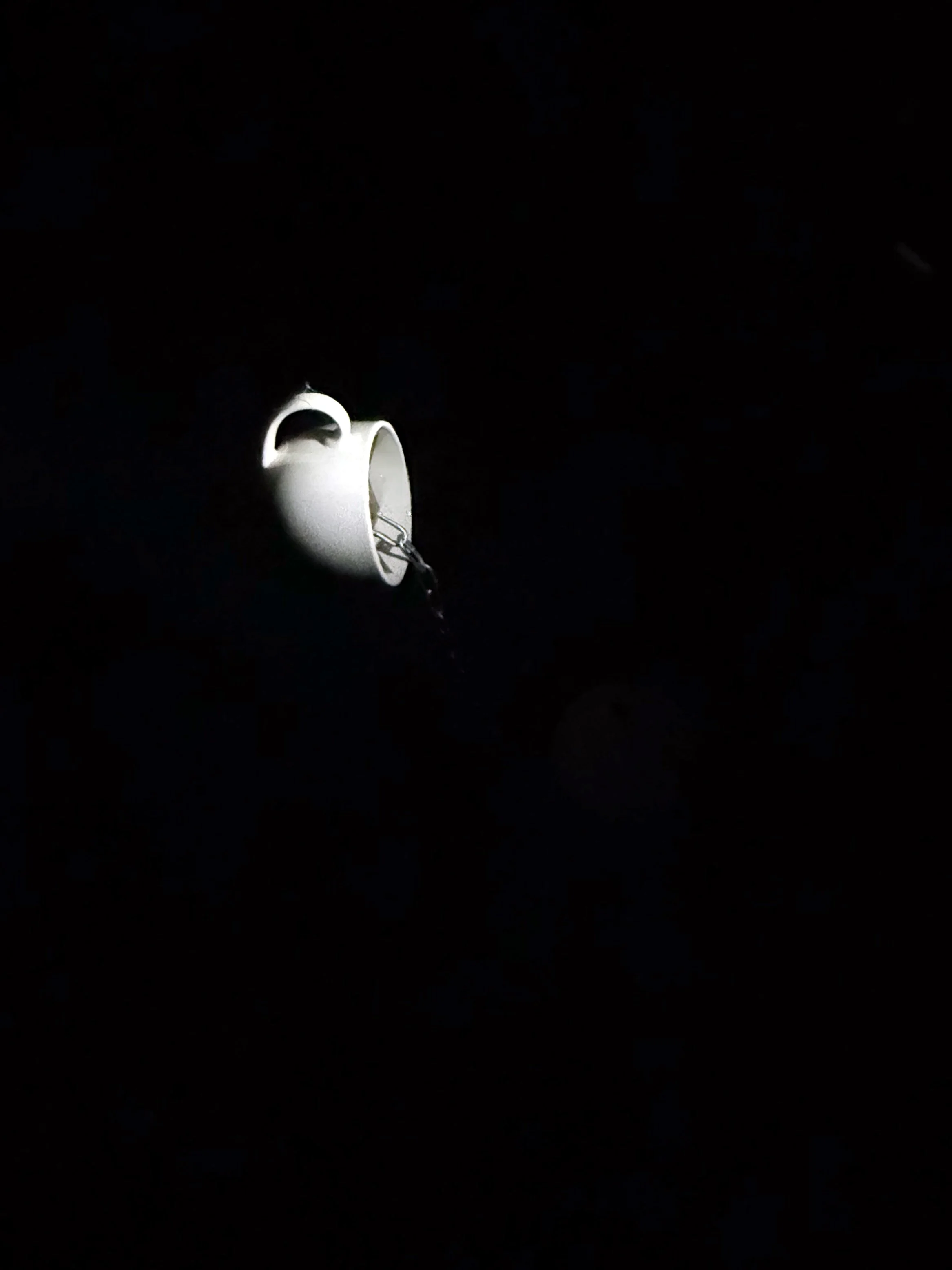 A white ceramic coffee mug turned on its side with a chain attached, placed against a black background.