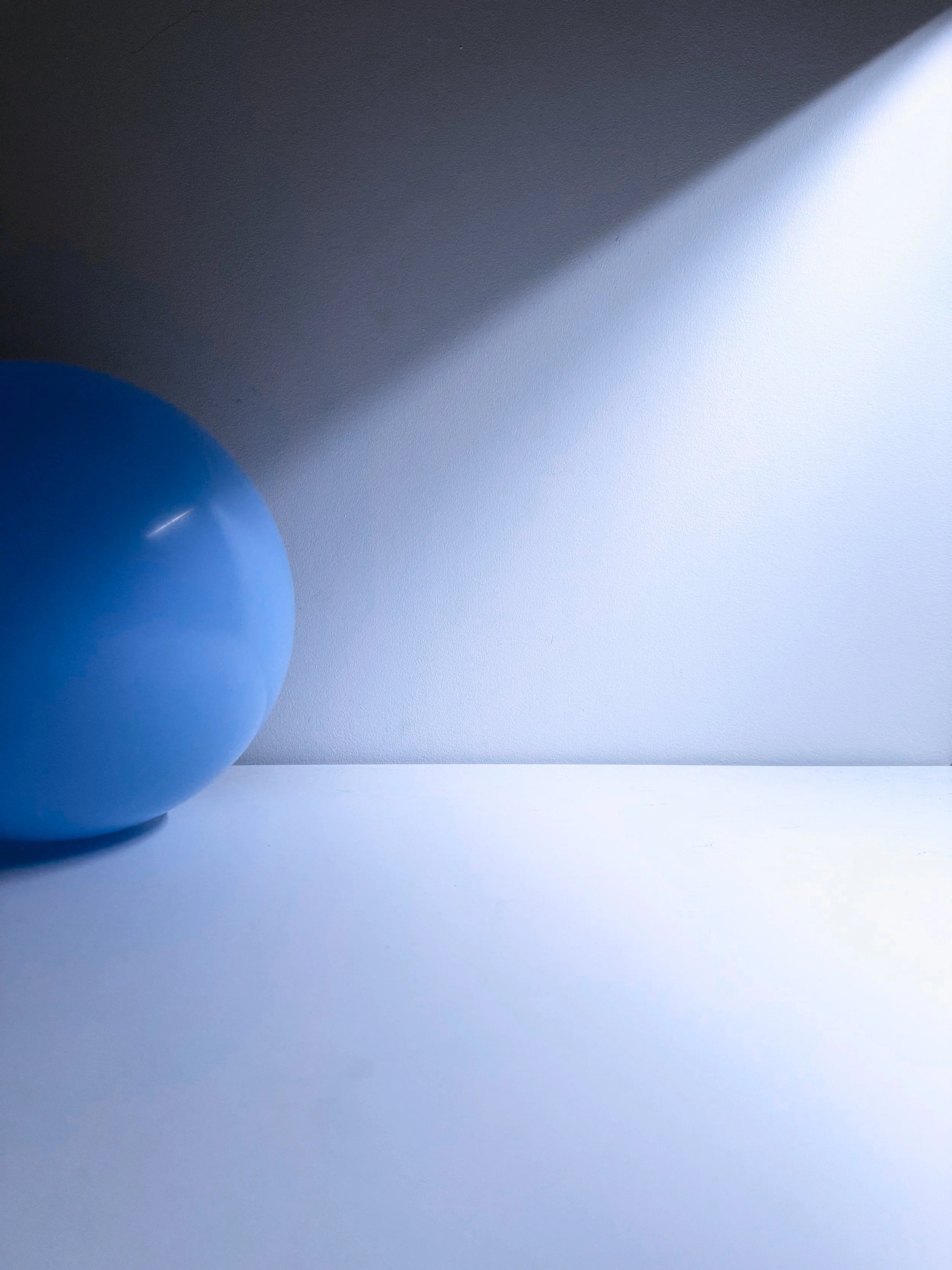 A blue balloon on a white surface with shadow and lighting effects.
