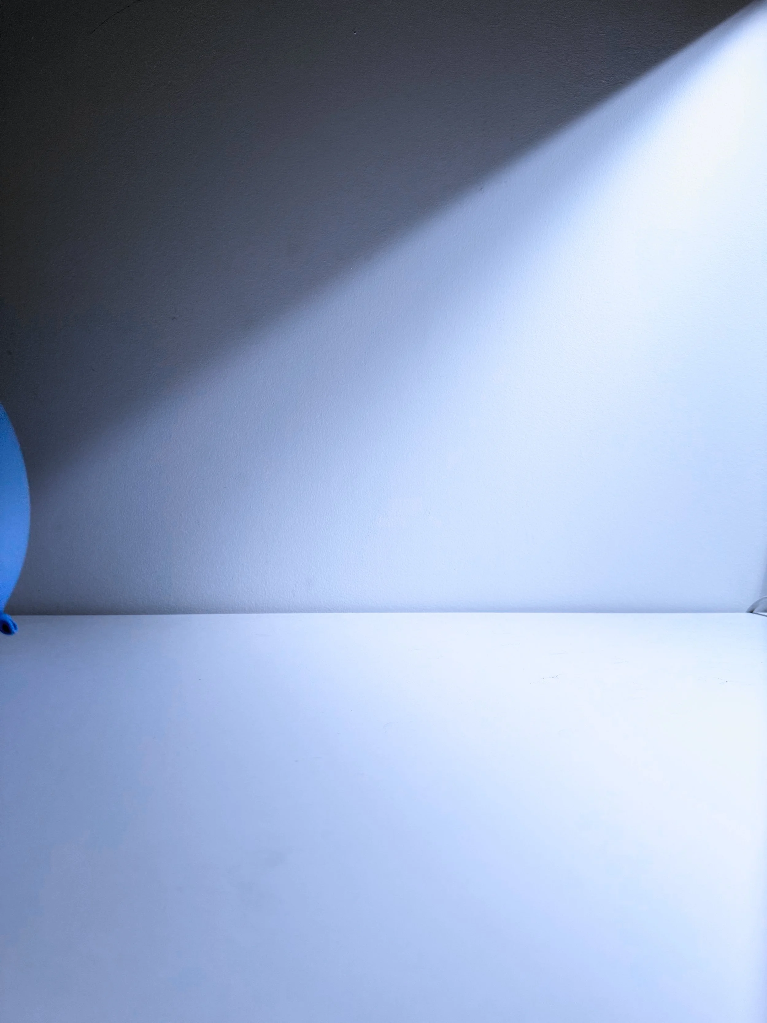 A portion of a blue balloon visible on the left side, against a plain white surface background with a large shadow cast from the top left corner.