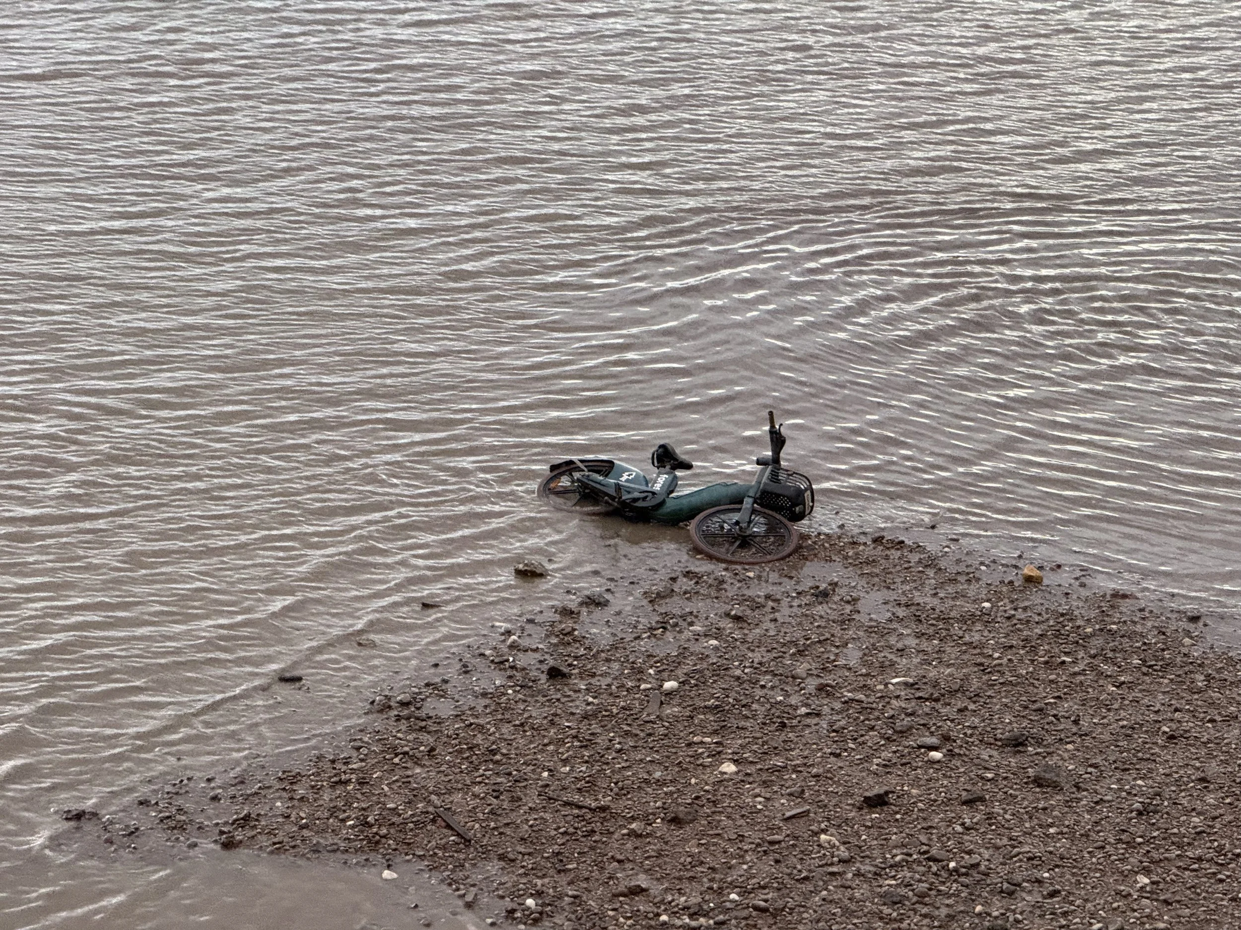 A bicycle lying on a rocky shoreline next to a body of water.