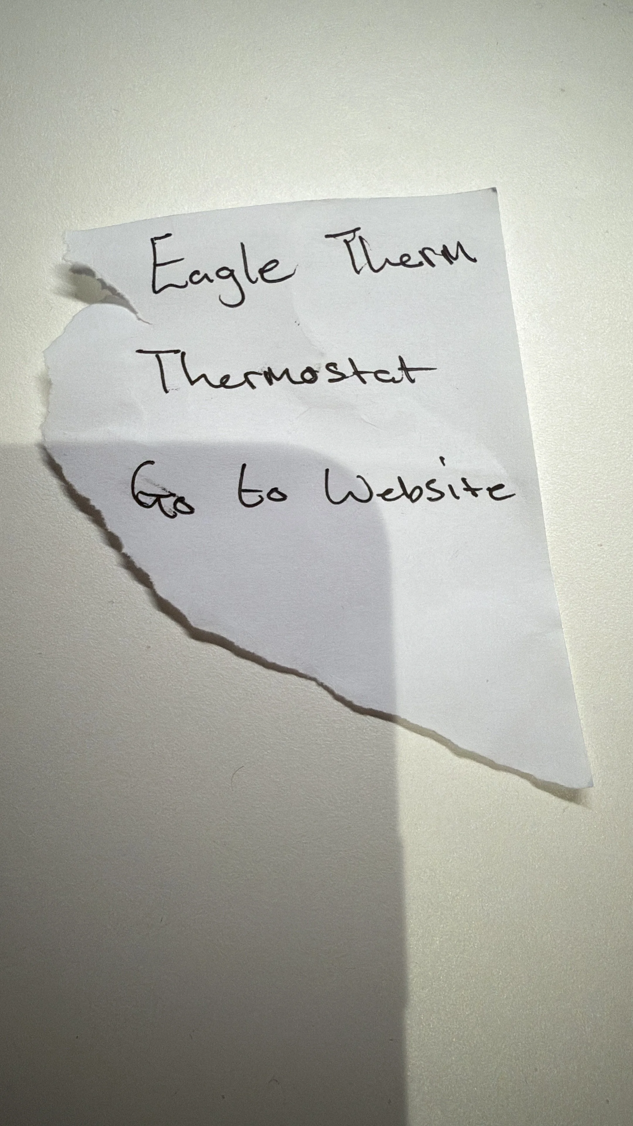 A torn piece of white paper with handwritten words: 'Eagle Therm Thermostat' and 'Go to Website'.