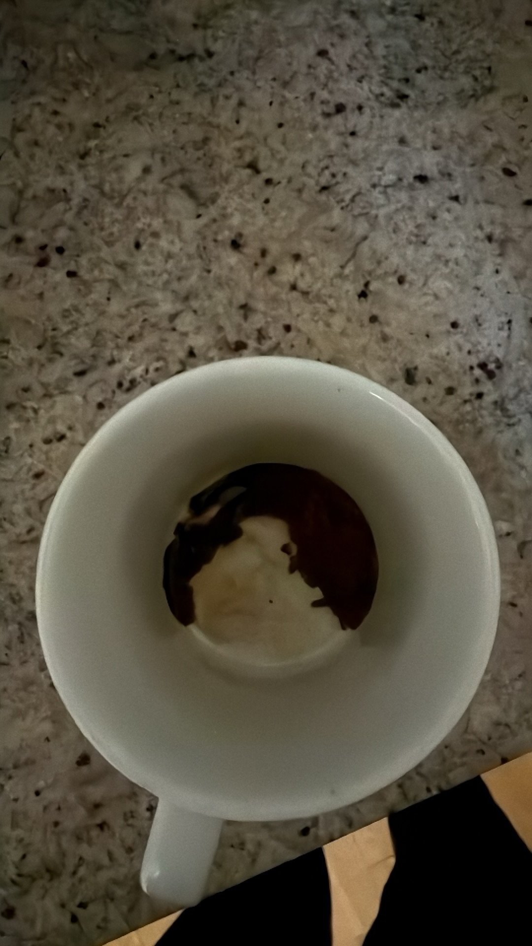 Coffee mug with dark coffee and cream on a speckled granite countertop.