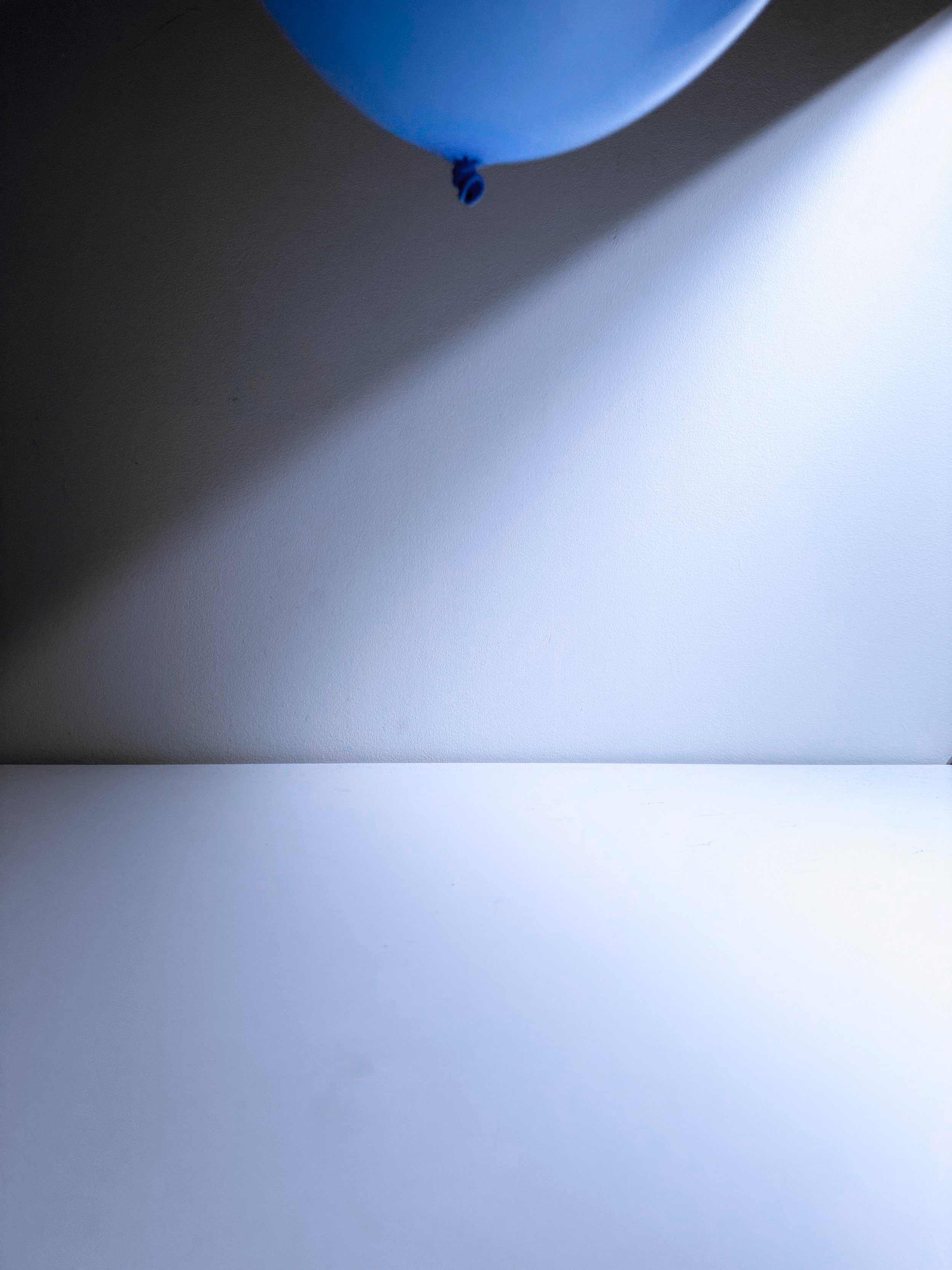 Blue balloon hanging from the ceiling casting a shadow on the wall.