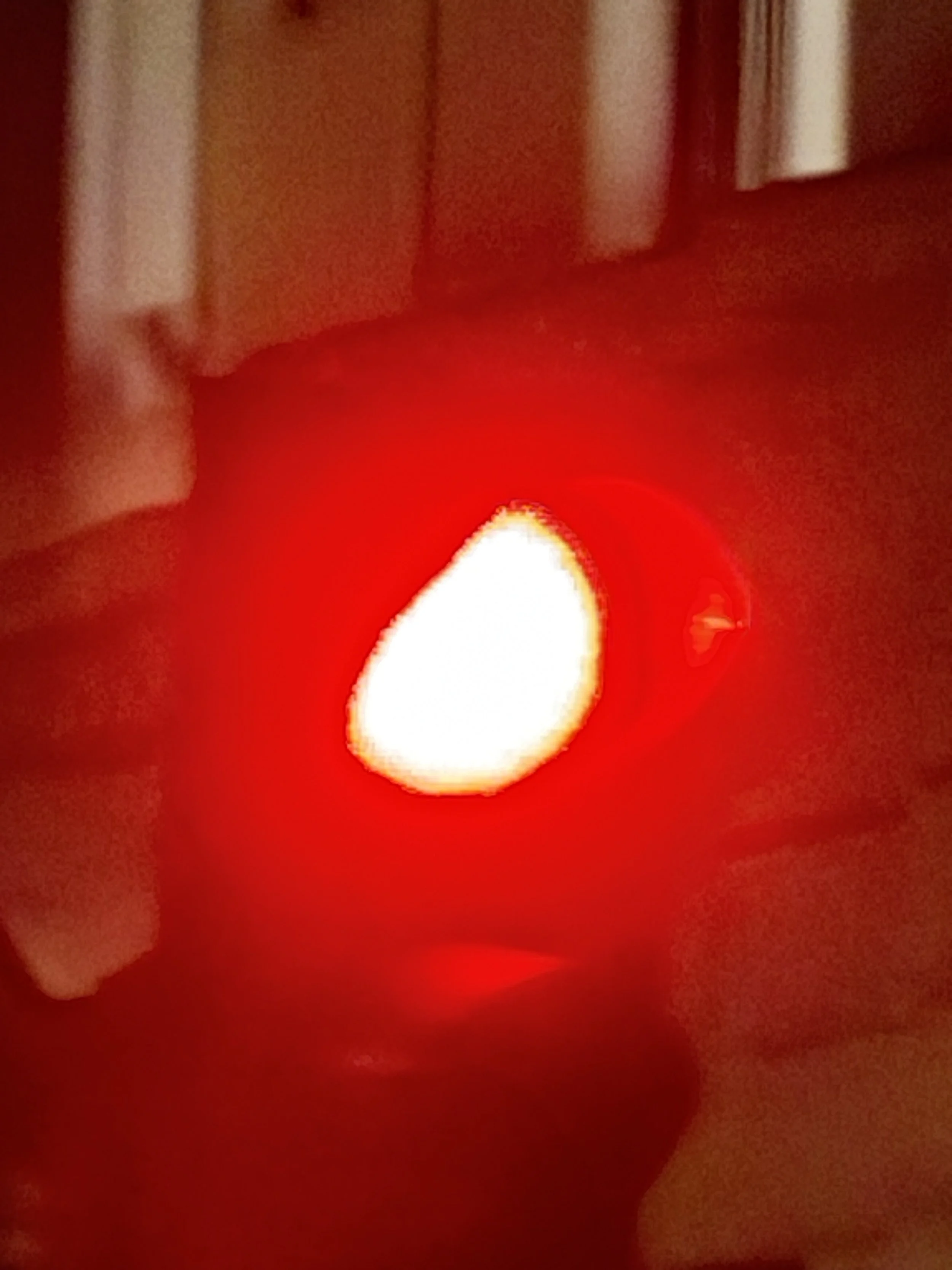 A red candle with a white flame illuminating a dark room.