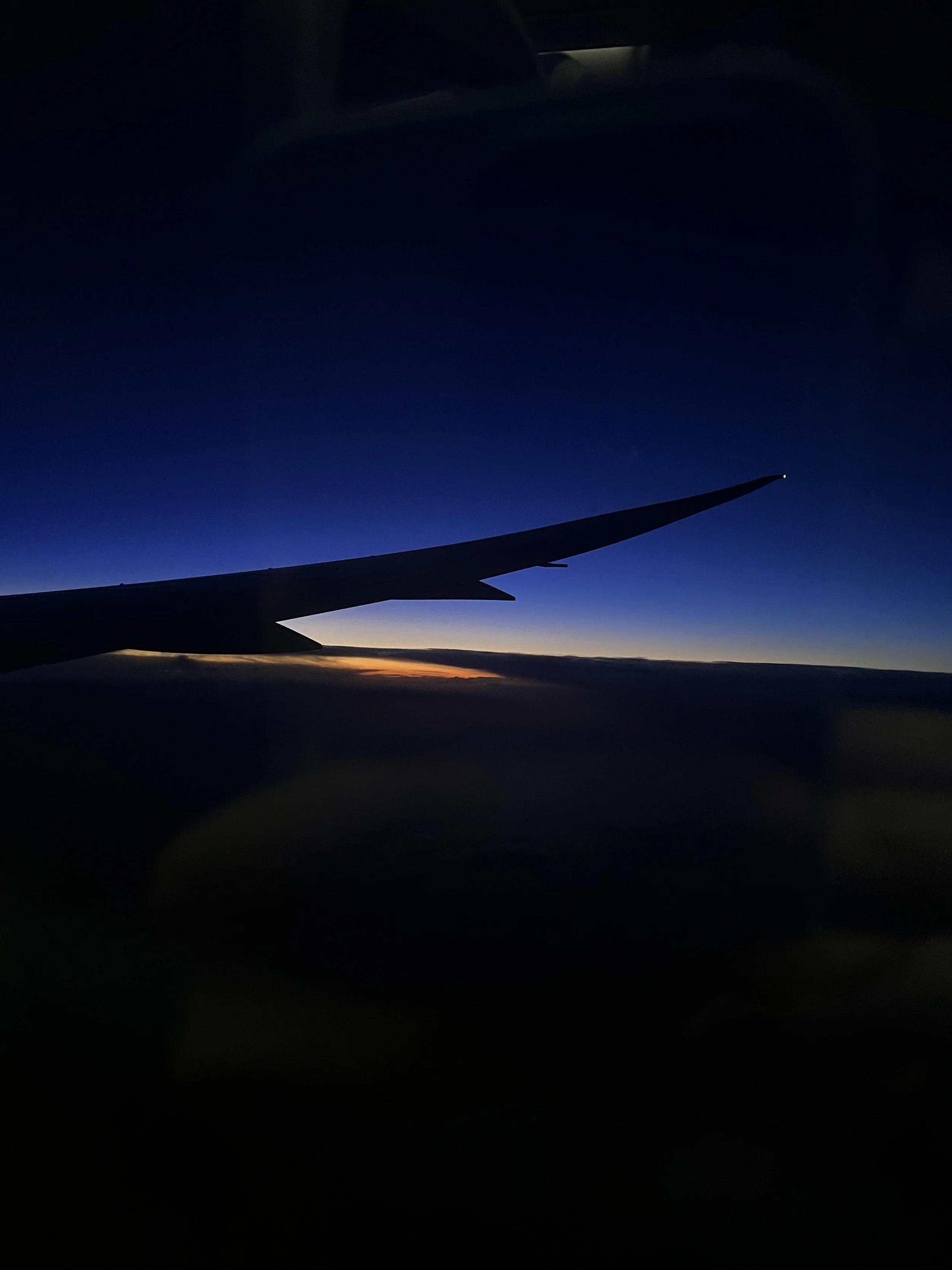 View of an airplane wing against a dark sky during sunset or sunrise, with the wingtip illuminated.