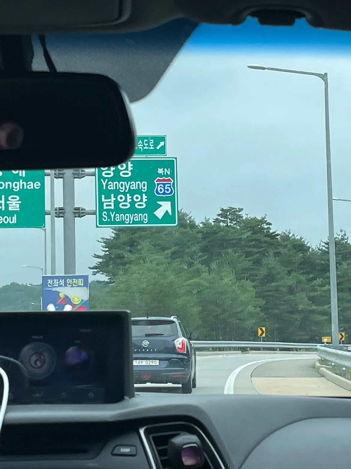 A highway with green directional signs in Korean and English, indicating routes to Yongyang, South Yongyang, and Seoul. Cars are visible on the road, and there is a street lamp and trees in the background.