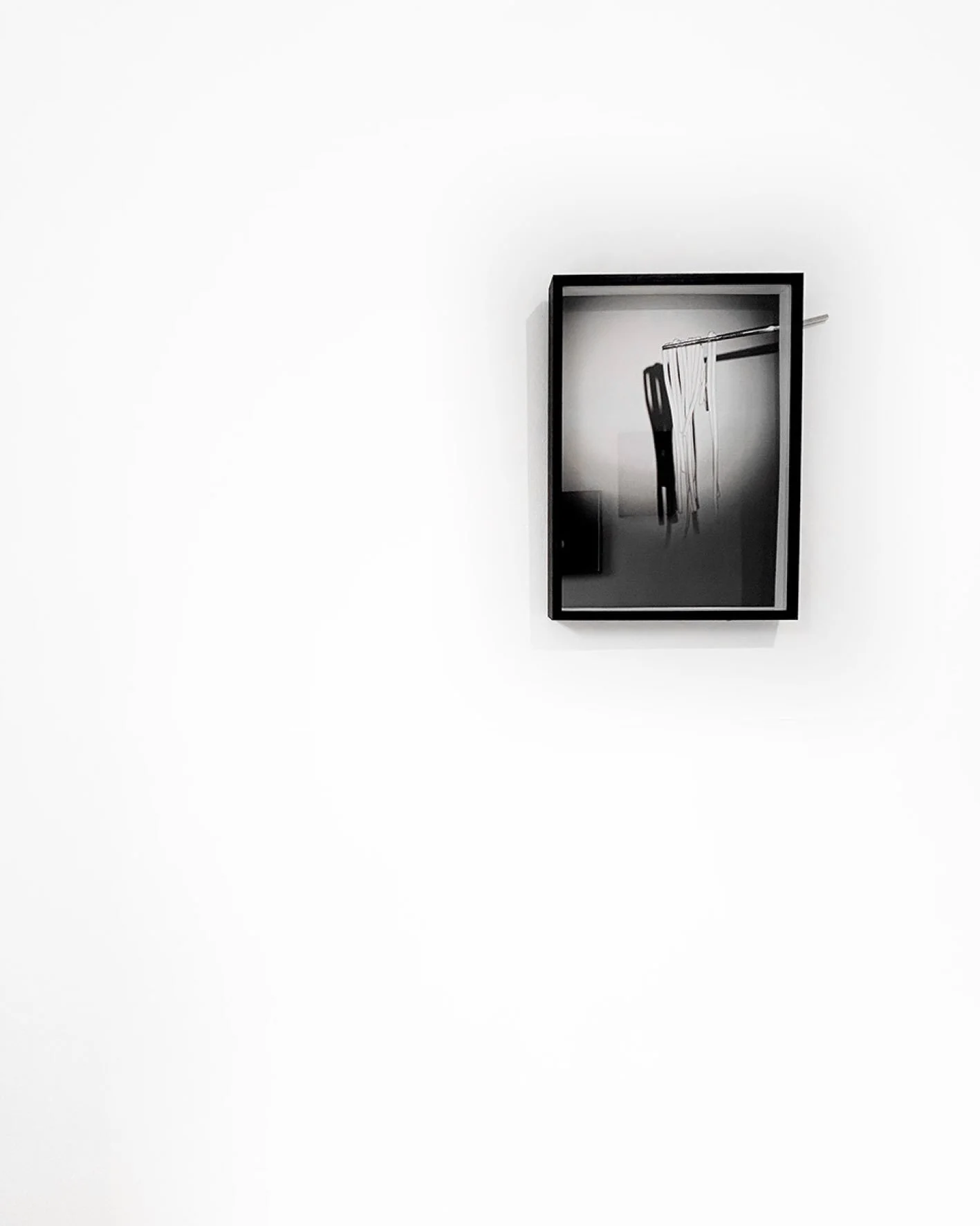 Mirror on a white wall reflecting a black chair and hanging white cloth or clothing