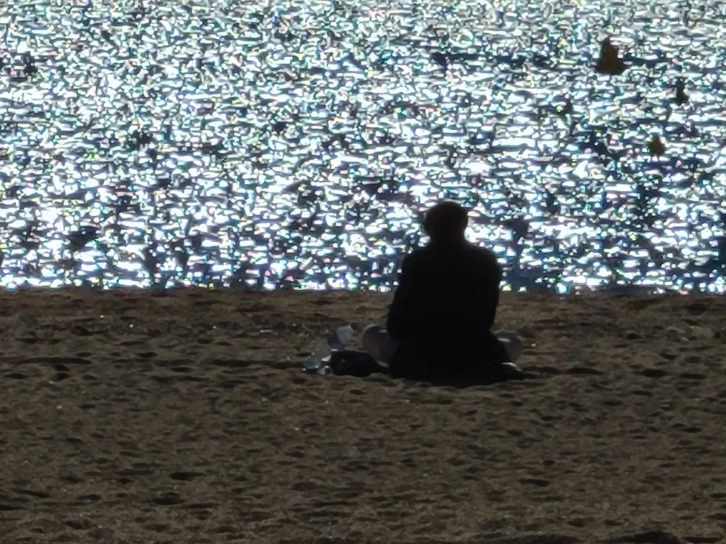 A person sitting on the ground at night and looking at shimmering, reflective surface, possibly water or a display.