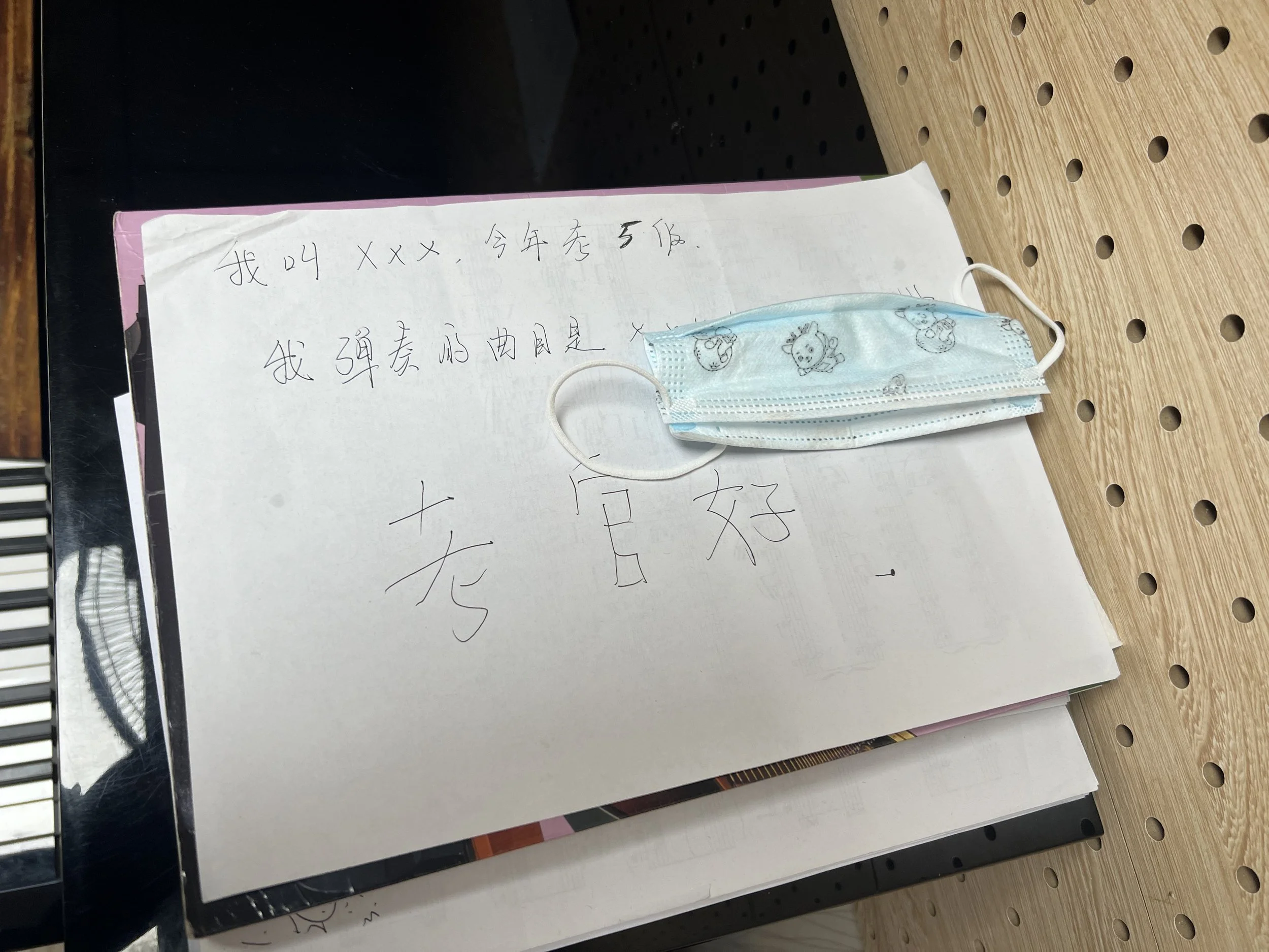 Handwritten note in Chinese with a face mask placed on top, on a wooden perforated surface.