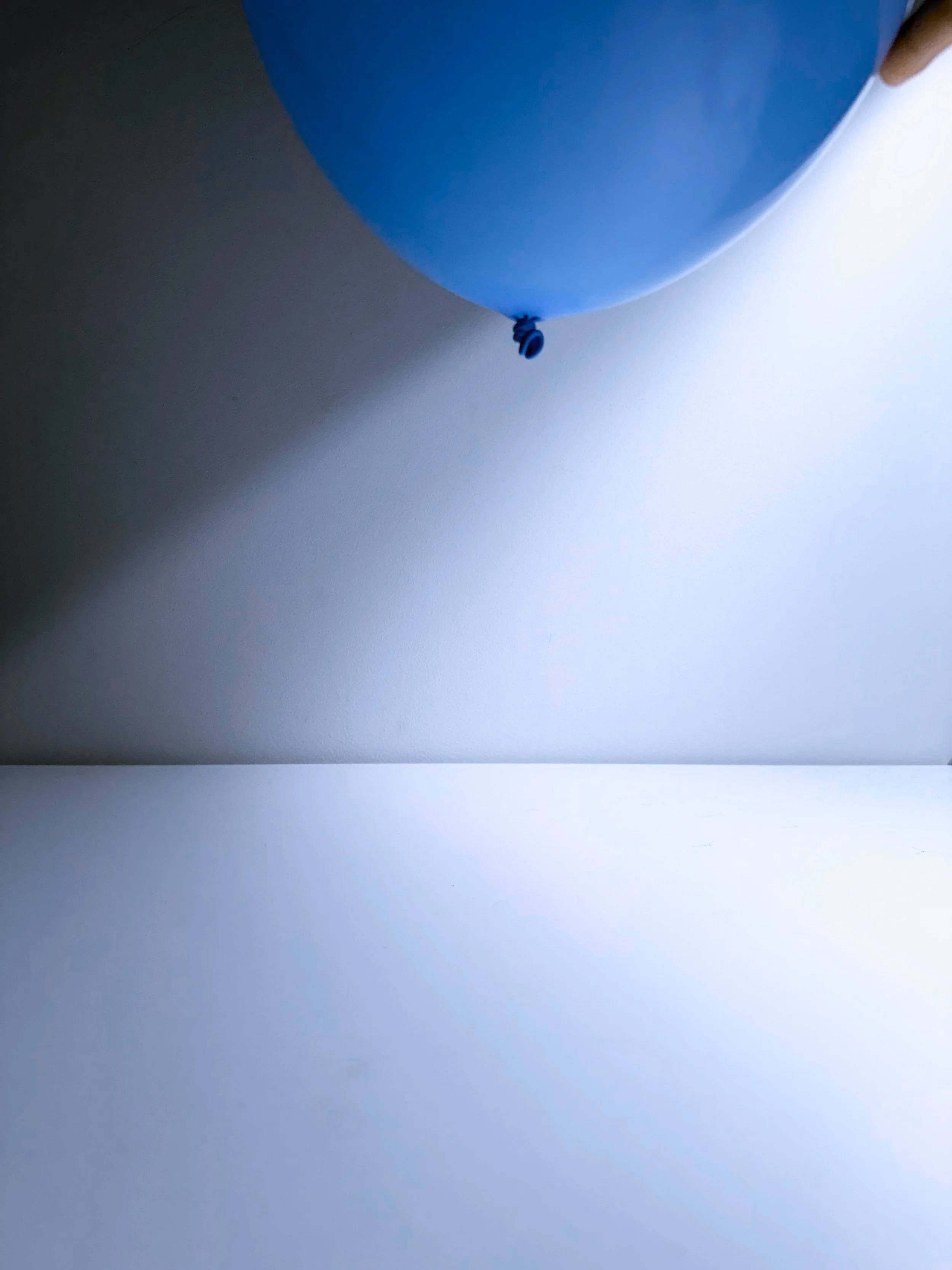 A blue balloon floating against a bright sky with some shadows and light reflections.