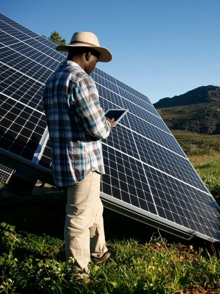 Farmer working in field next to solar panel and holding tablet