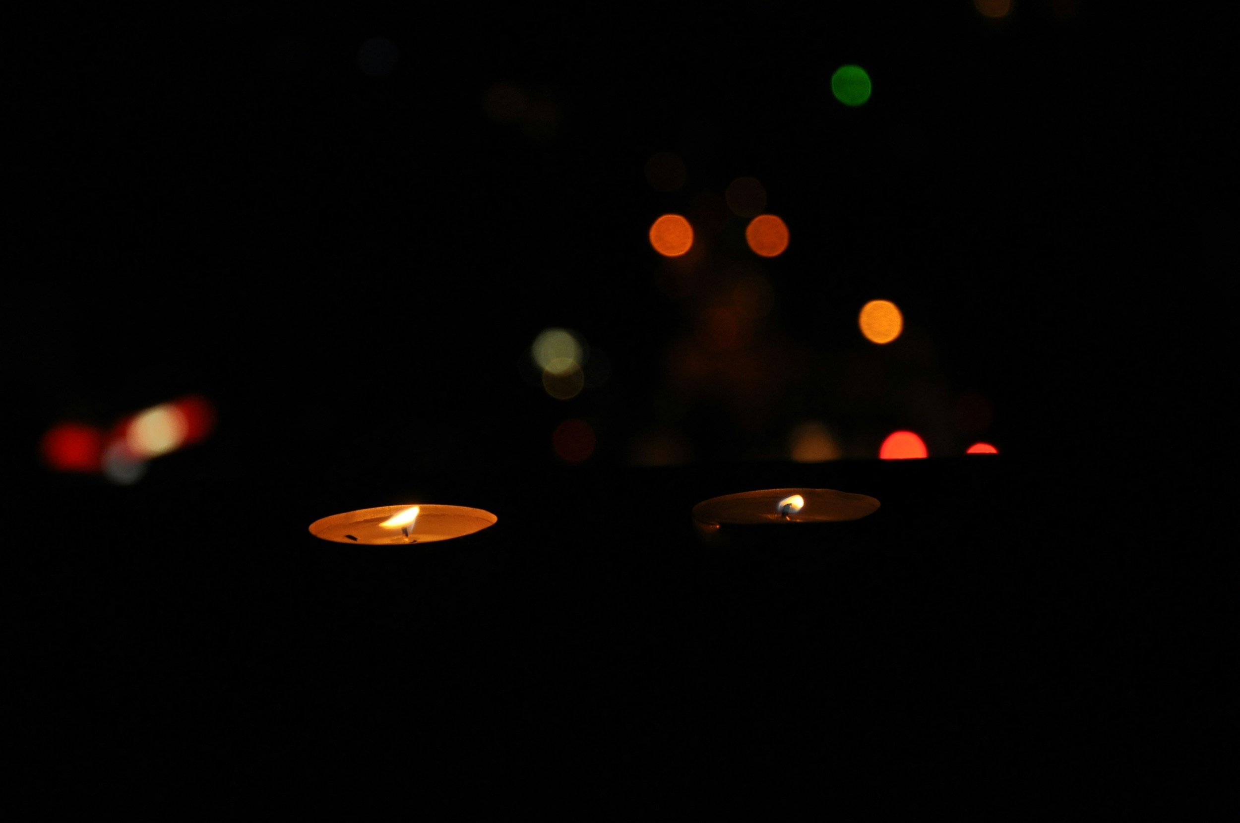 Dark night scene with several lit candles and blurred colored lights in the background.