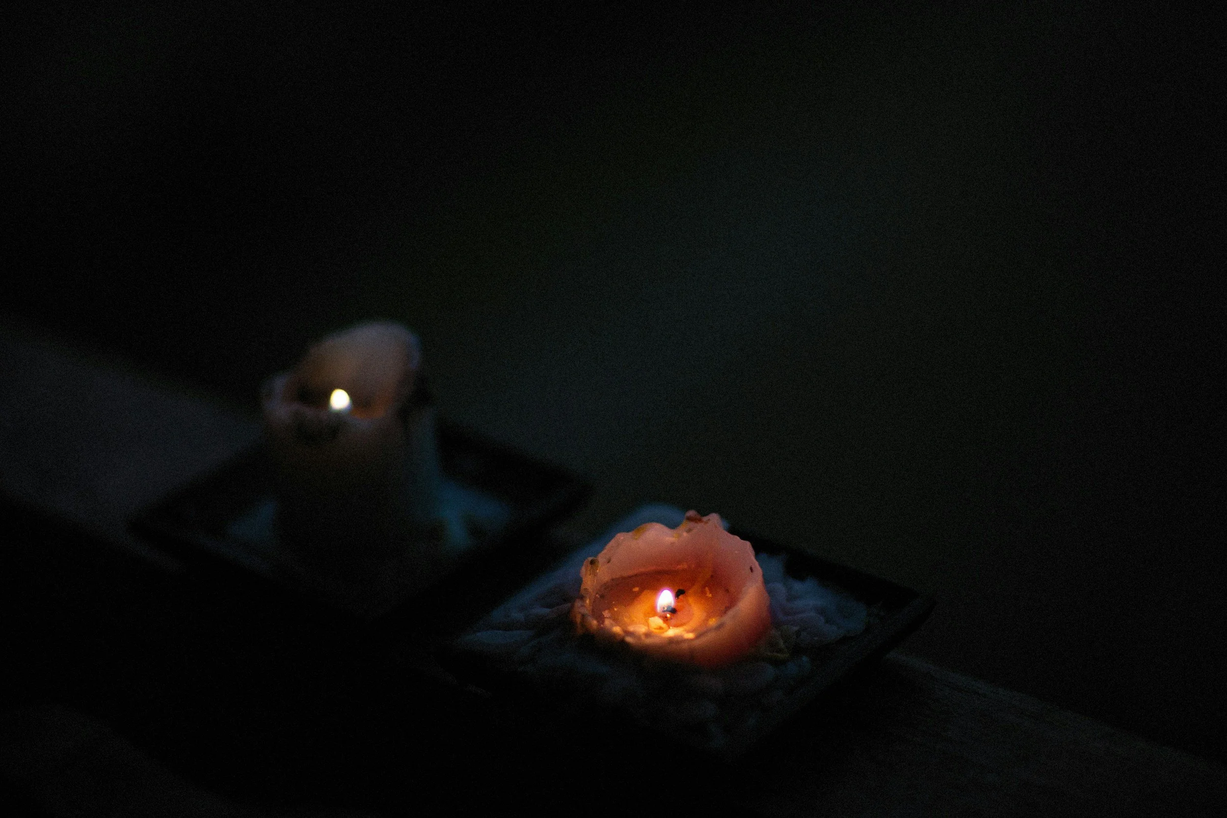Close-up of lit candles in a dark setting, some with melted wax, creating a warm, soft glow.