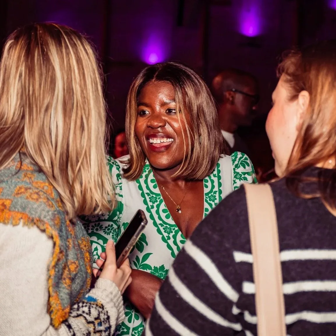 Three women having a conversation at an indoor event, with purple lighting in the background.