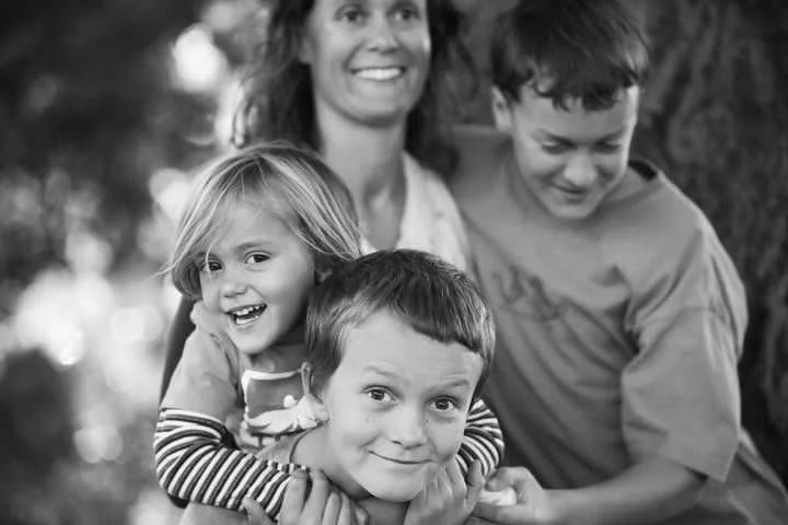 A woman with three children outdoors, smiling, with a tree in the background