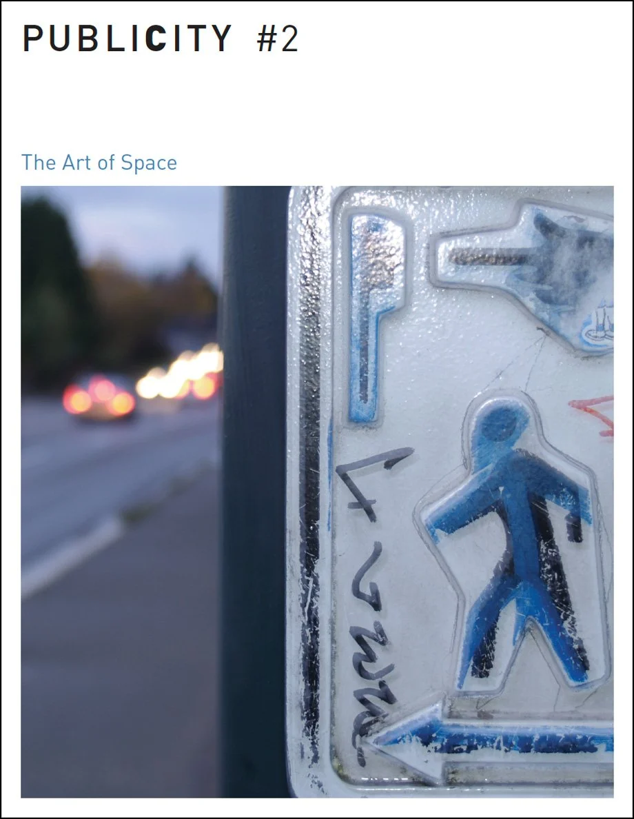 Close-up of a weathered blue pedestrian crossing sign on a street, with blurred cars and traffic lights in the background.