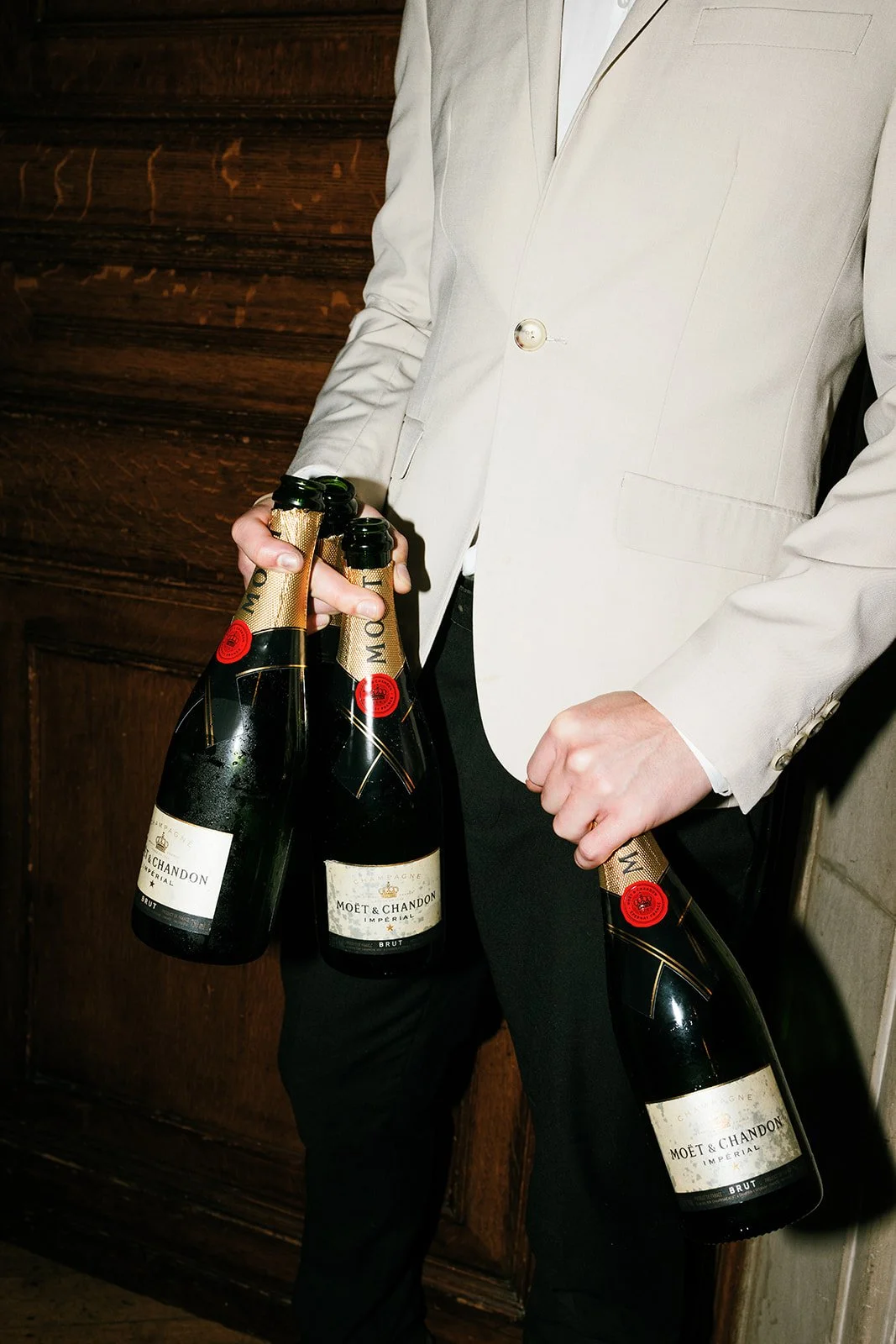 Man in a white blazer holding three bottles of Moët & Chandon champagne.
