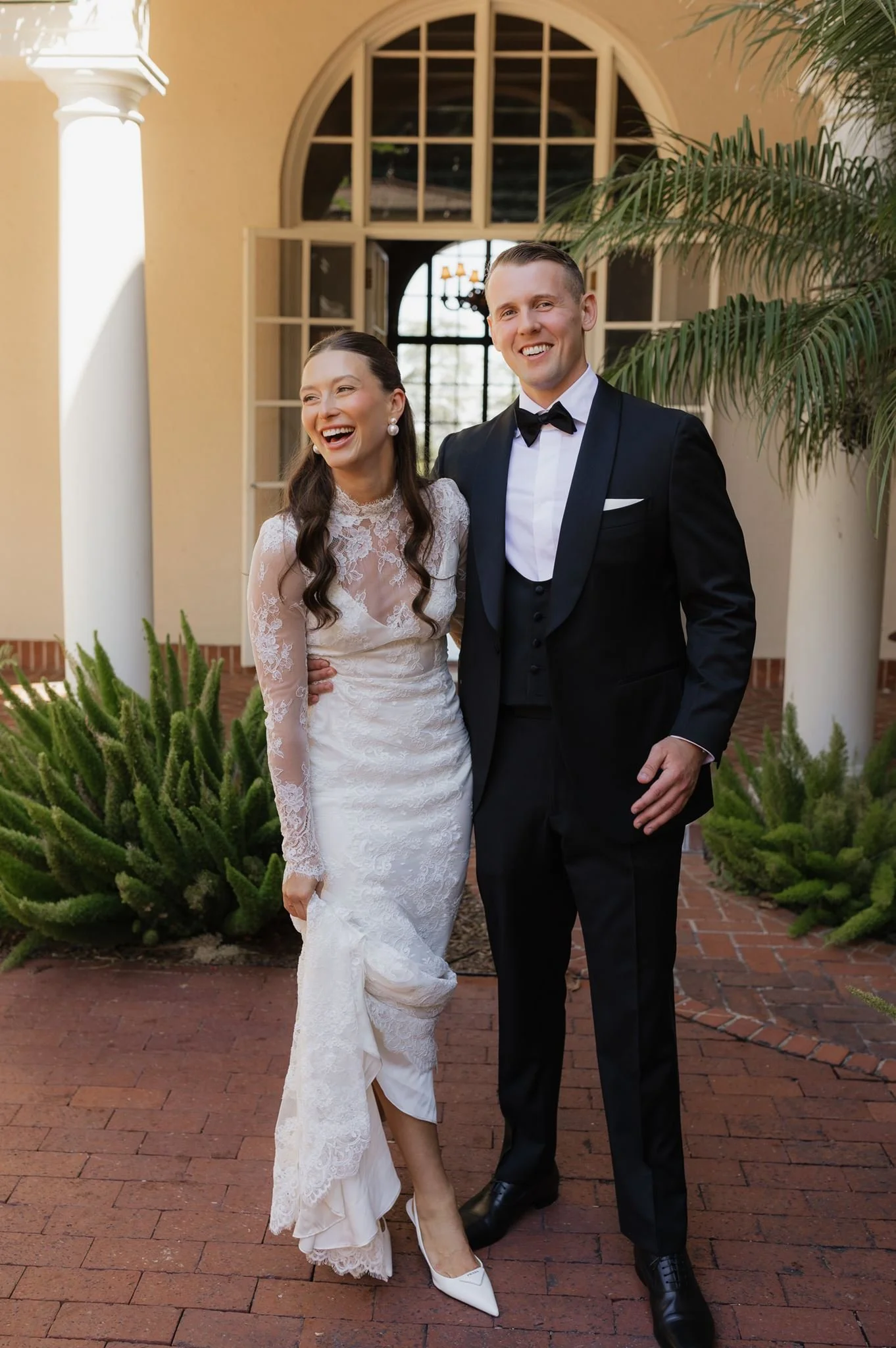 A stylish bride and groom smiling outside Villa Montalvo in California.