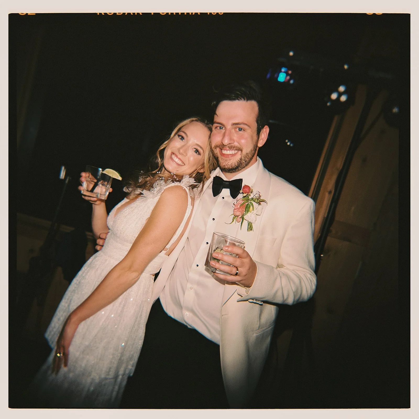 A film photo of a bride and groom dancing and holding drinks.