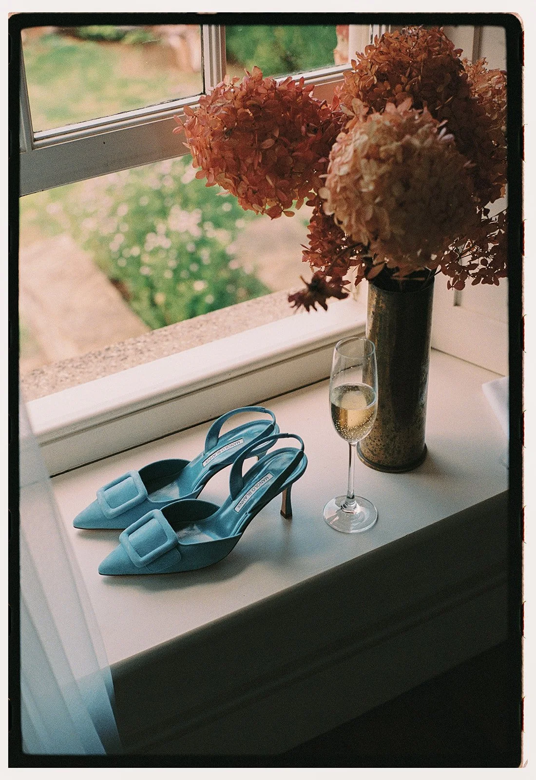 A film photo of blue suede wedding heels and hydrangeas on a window sill in the Cotswolds.