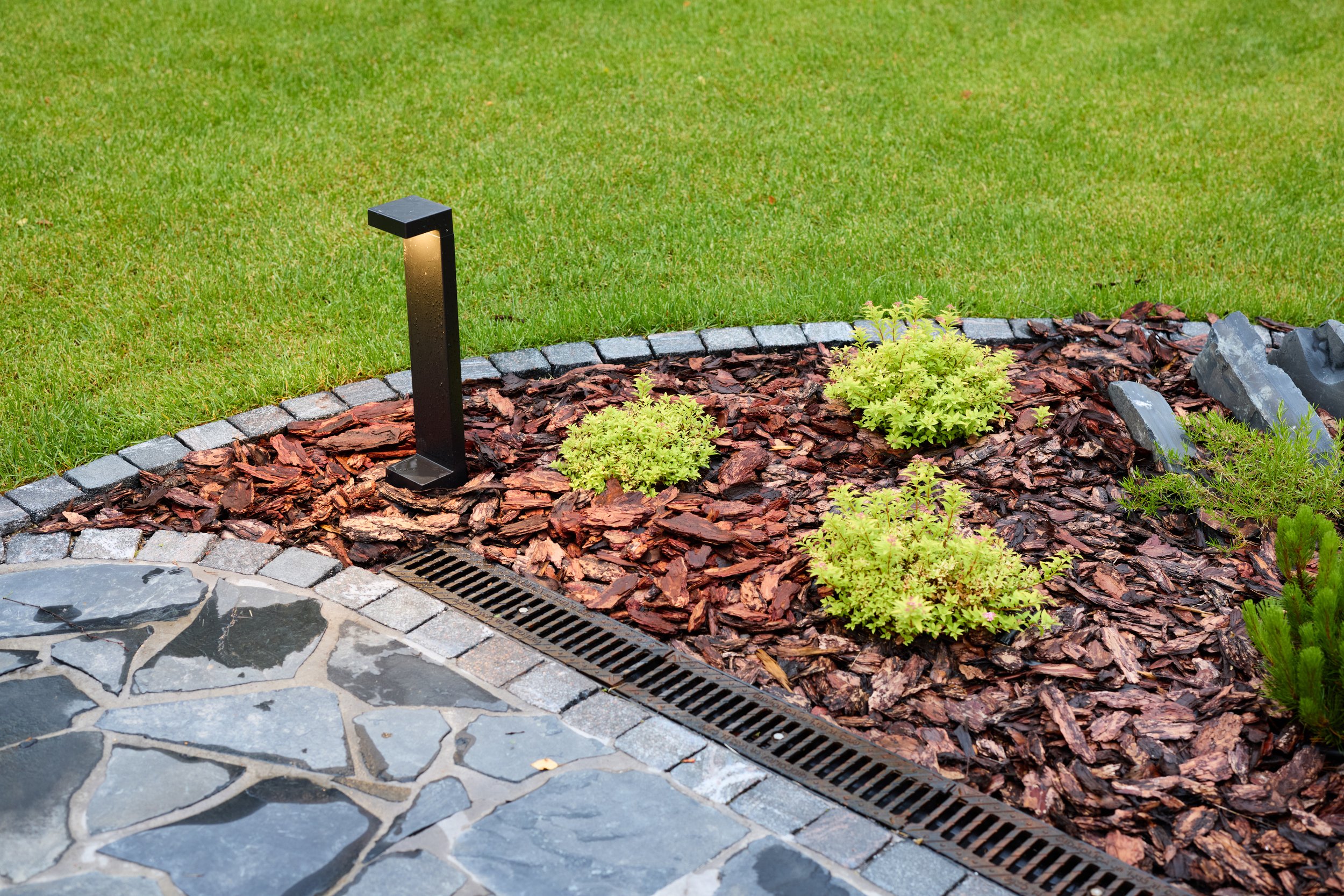 Outdoor lighting lighting the landscape and a garden bed next to a lawn that is green from sprinklers watering it